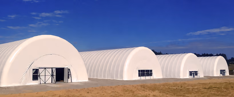 Four white fabric-covered arched storage warehouses under a blue sky on dry ground.