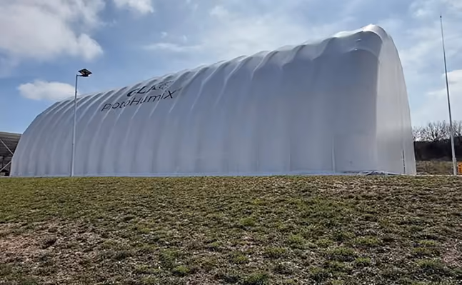 Large white inflatable structure with 'Protohumix' text outdoors on grassy ground under blue sky.