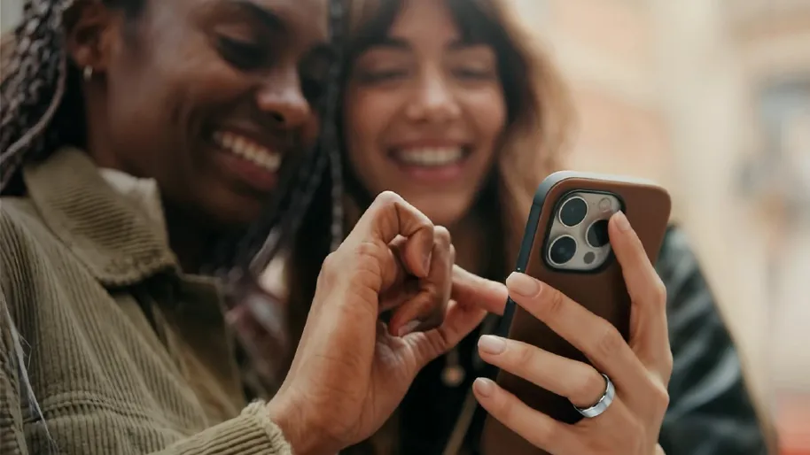 Two young ladies one of whom is wearing a leep smart ring and holding her smartphone. They are both looking at the smart phone screen and smiling in a relaxed manner