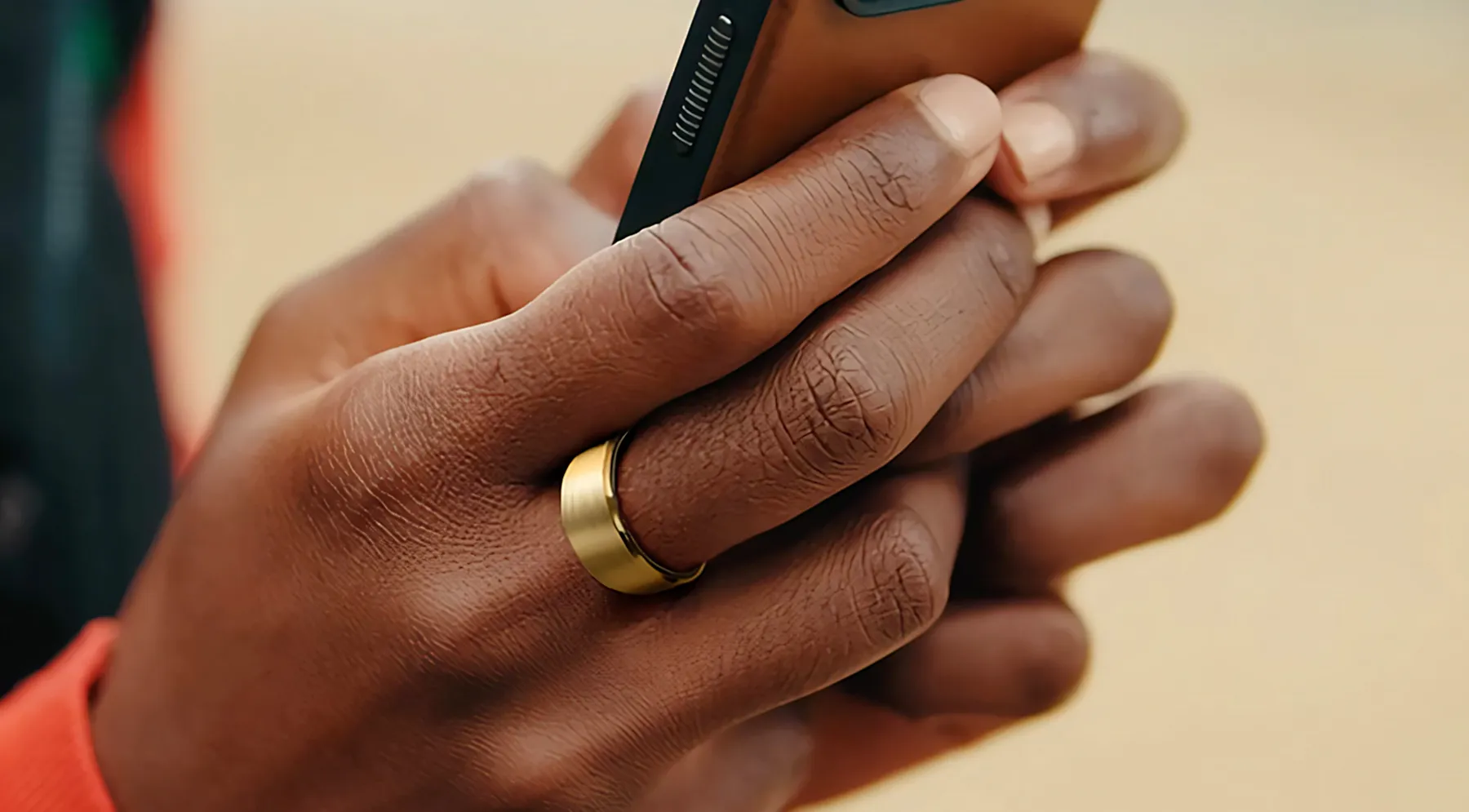 A close up image of a pair of hands holding a smartphone with a gold leep ring on the middle finger of their right hand.