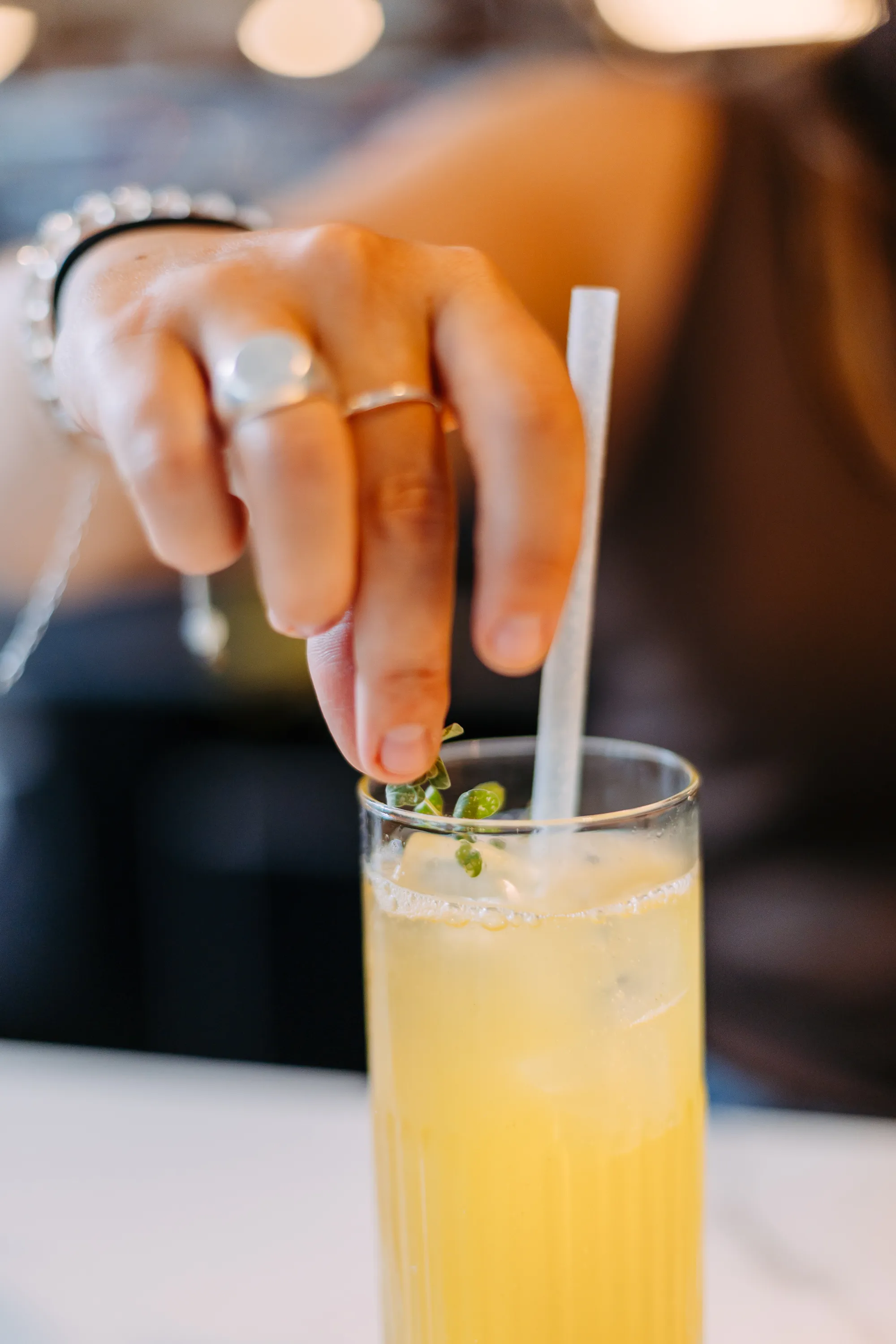 A yellow drink being prepared with herbs in it and a white straw