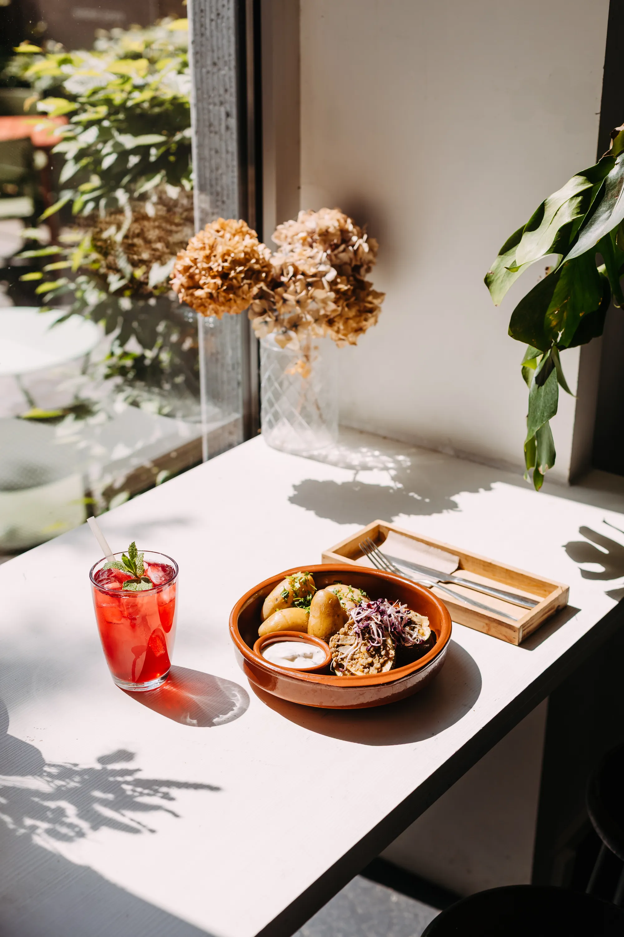 A dish served in the sun near the window with a red drink