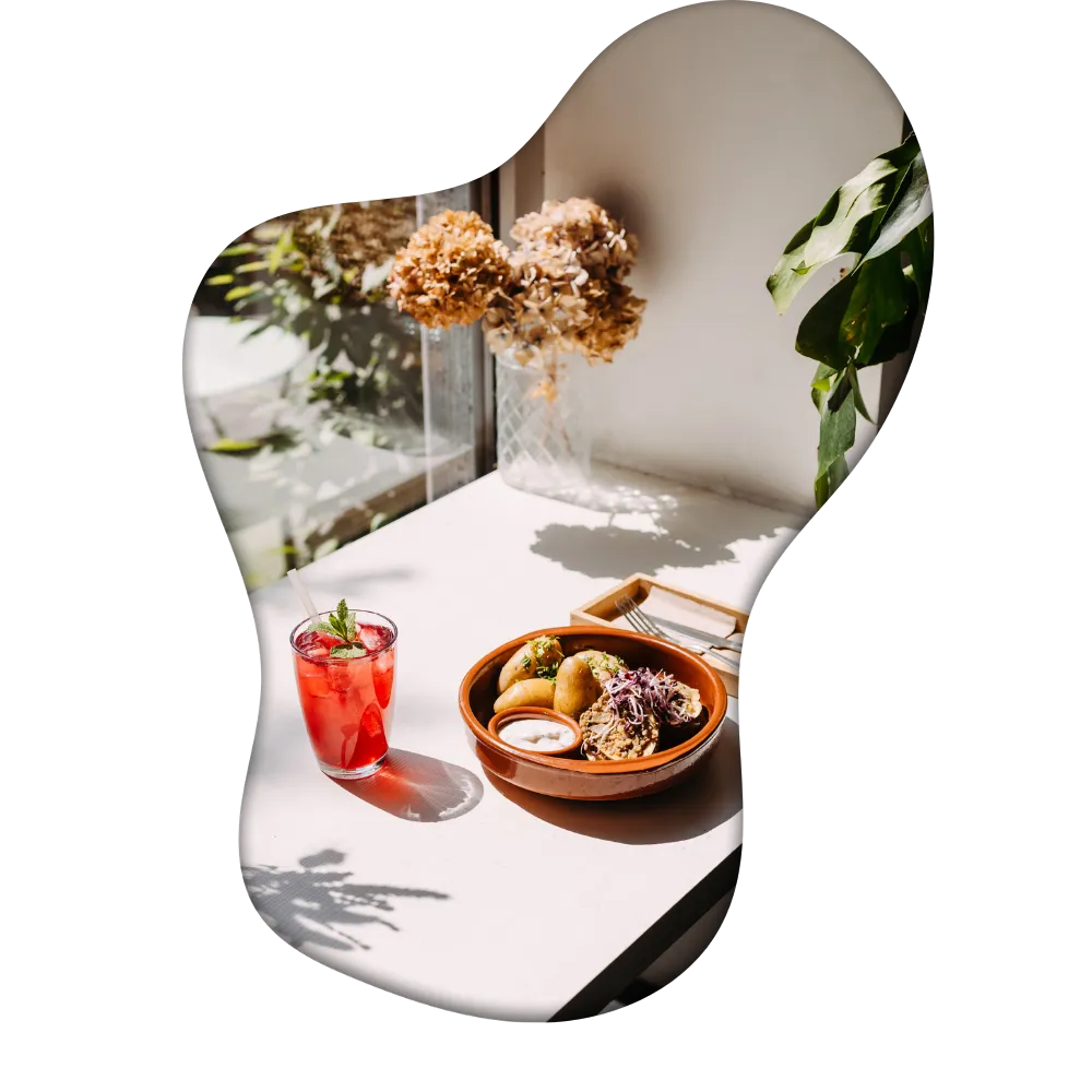 A well set table near the window with plenty of sunlight, a nice drink and a delicious meal