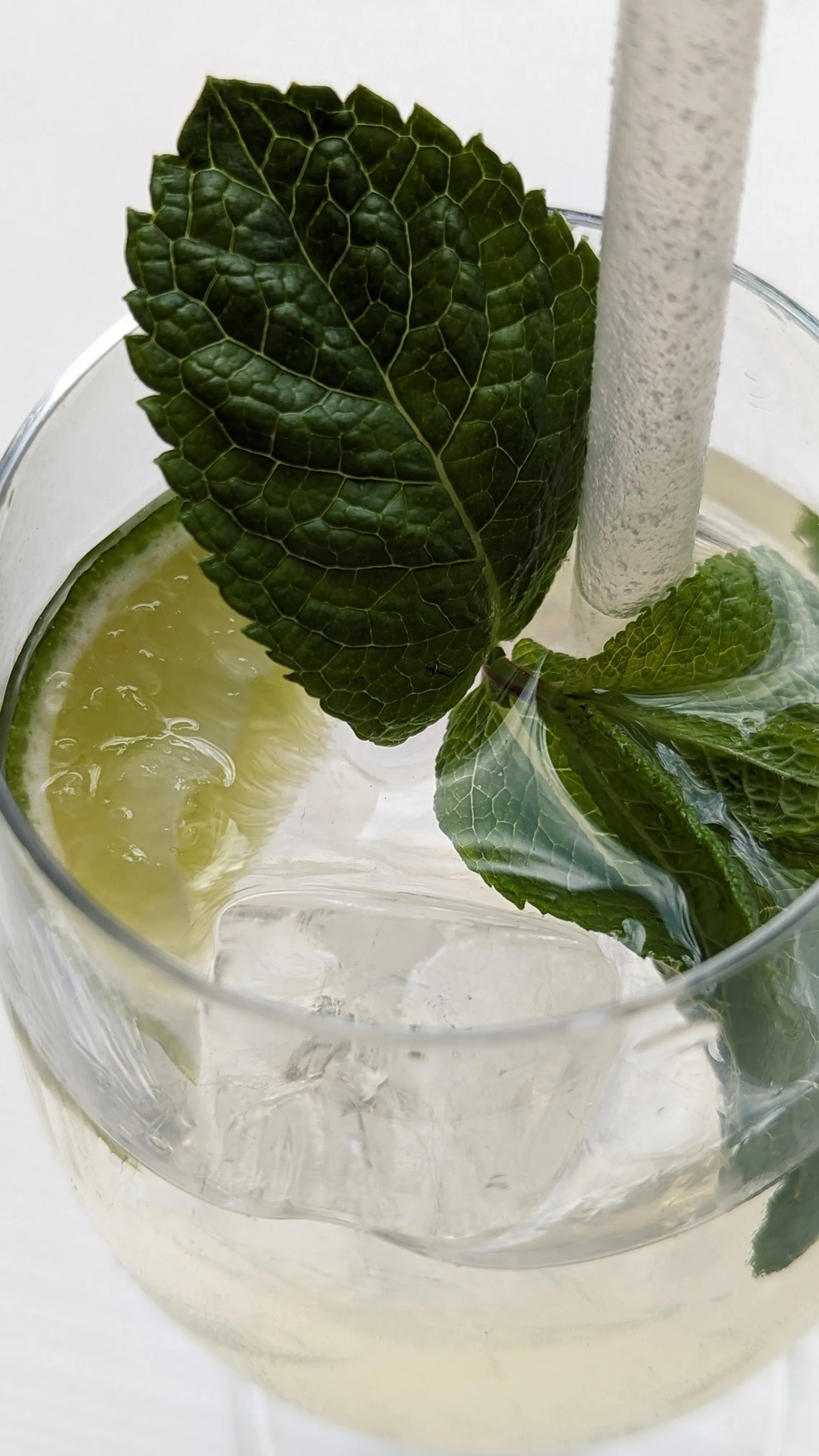 A drink with lime and mint in it with a white straw