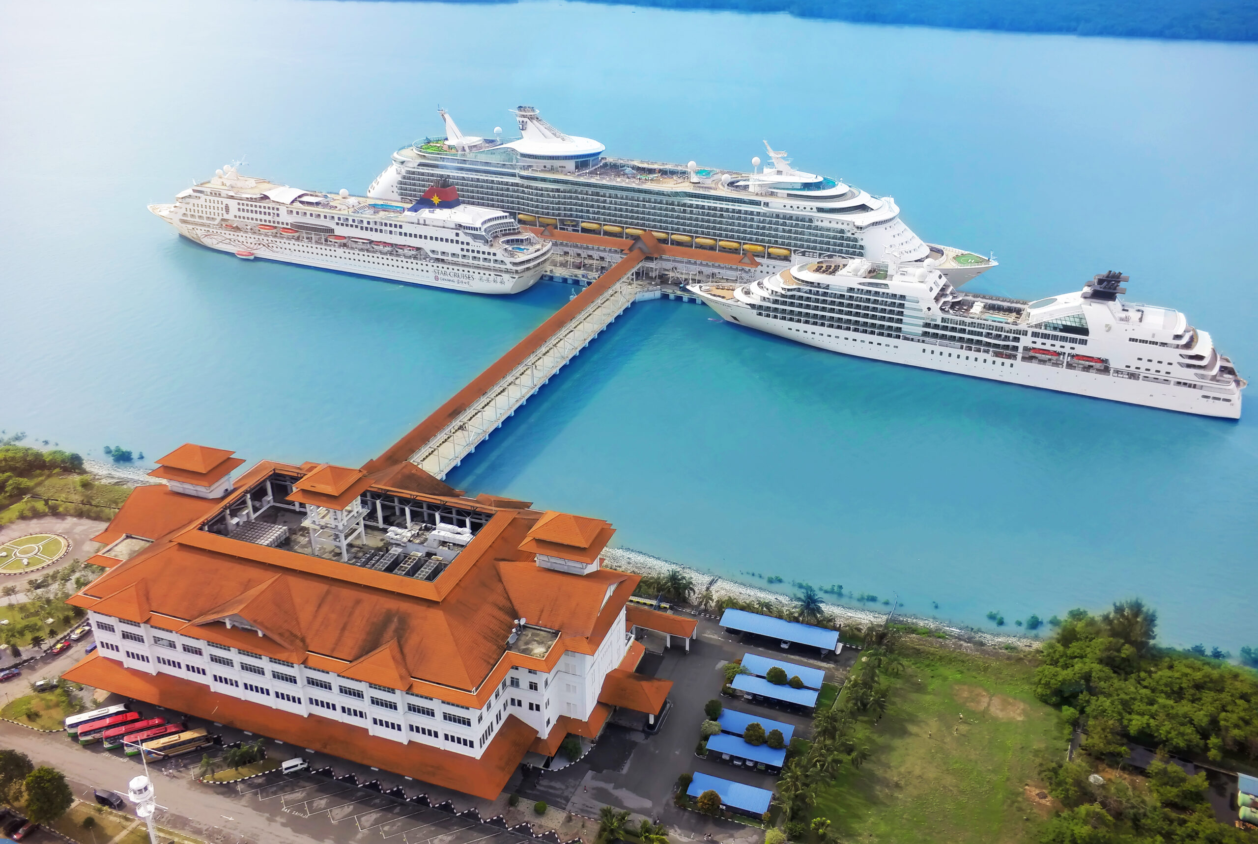 Large cruise ships docked at Port Klang Cruise Terminal with orange building by turquoise water