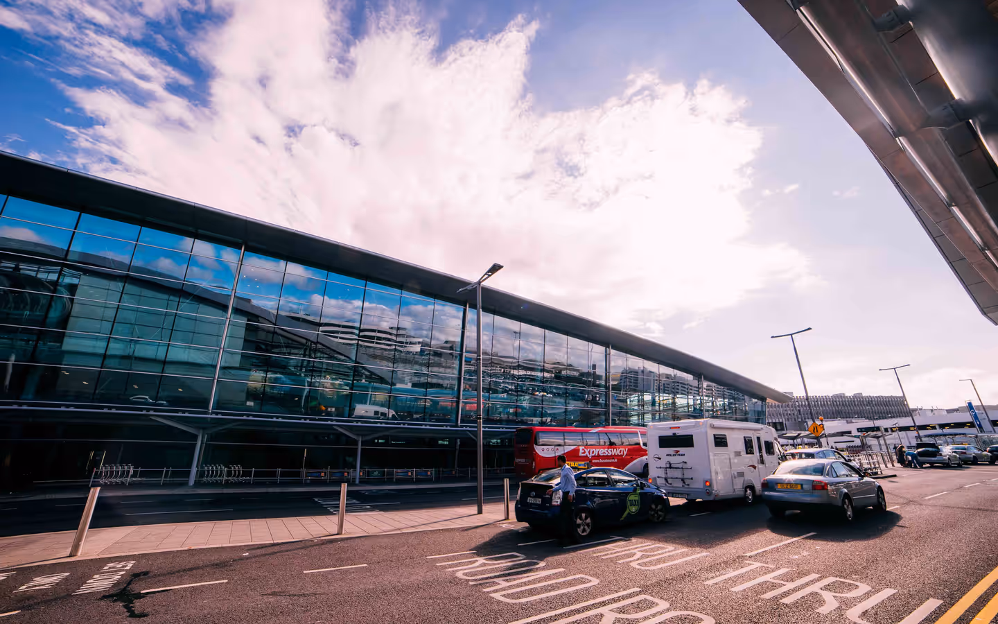 Daytime view of the modern terminal building at Dublin Airport, Ireland, with cars and buses parked outside.