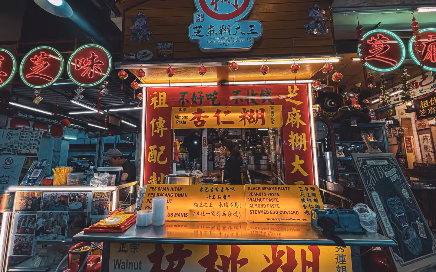 Authentic Malaysian street food stall in a Kuala Lumpur market, vibrant signage and lighting.