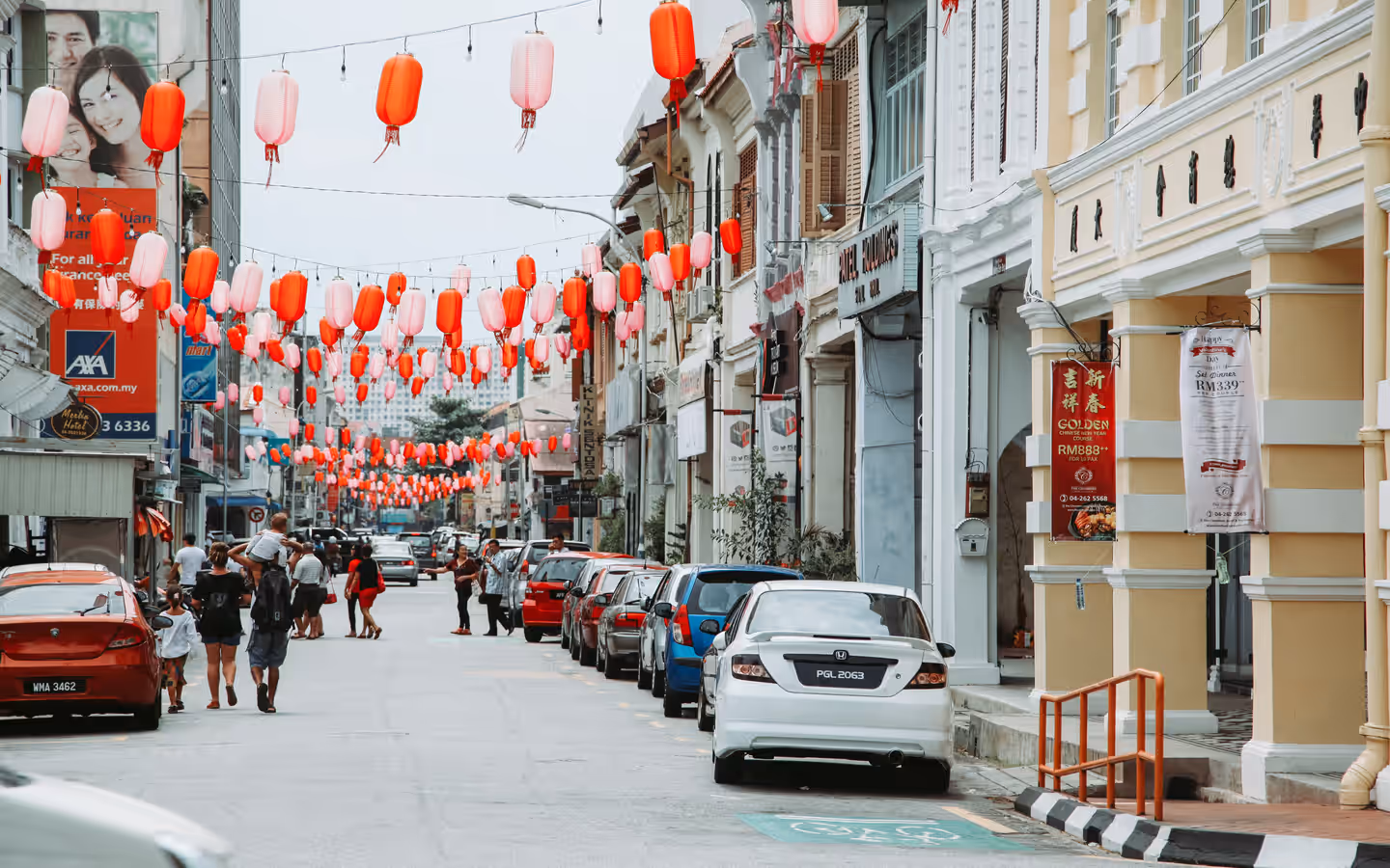 Crowd of people strolling on asphalt road with parked cars on street with residential buildings and hanging Chinese lanterns in city