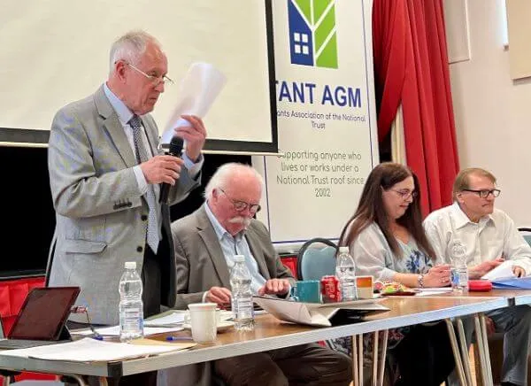 Speakers and attendees at the National Trust AGM event, with a man holding a microphone addressing the audience from the podium.