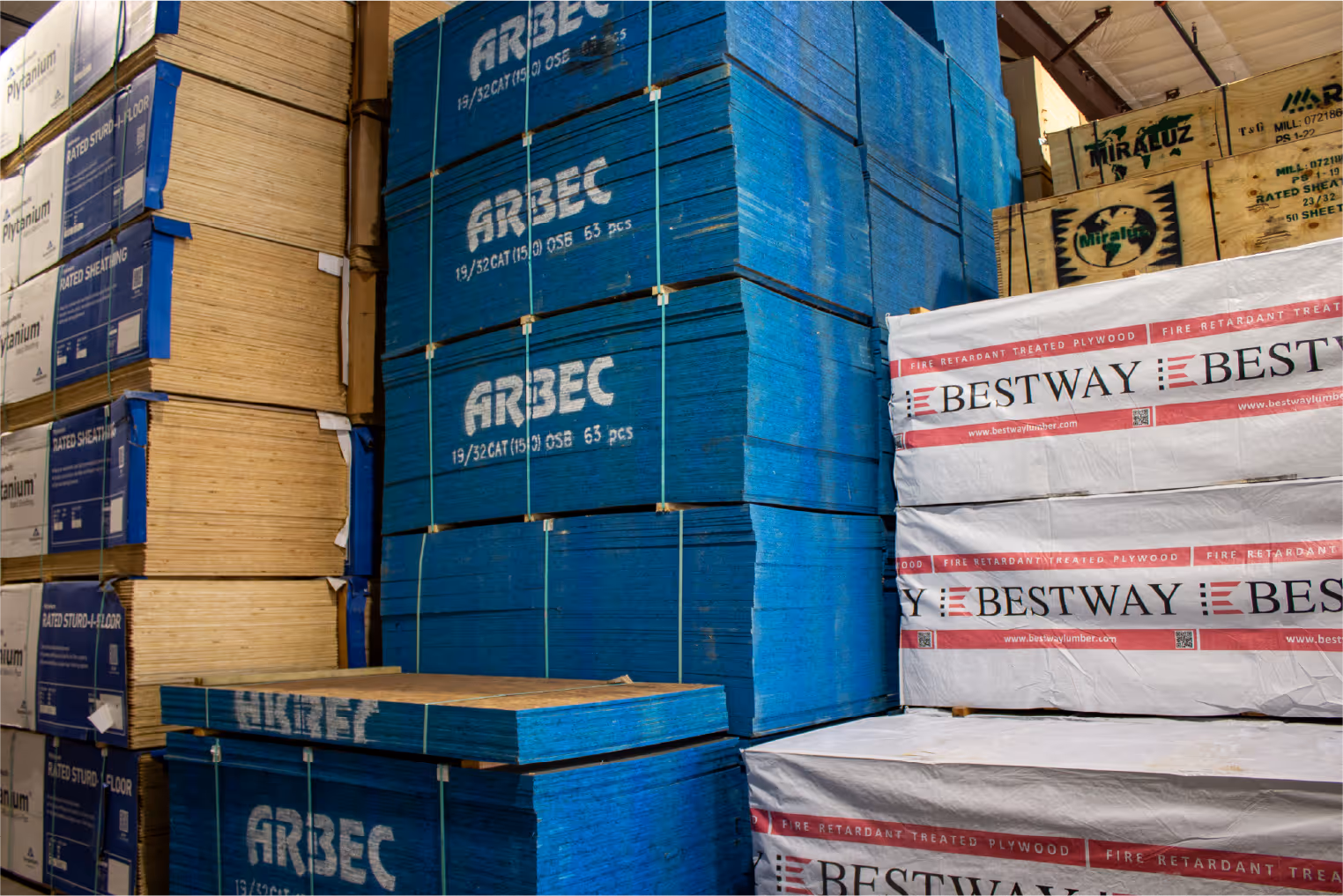 Stacks of plywood sheets and panels labeled ARBEC and BESTWAY in a warehouse.