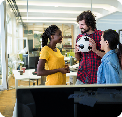 Three colleagues in an office, one holding a soccer ball, smiling and talking.