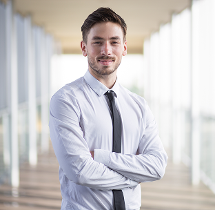 Young man in a white shirt and black tie standing with arms crossed in a bright, modern hallway.