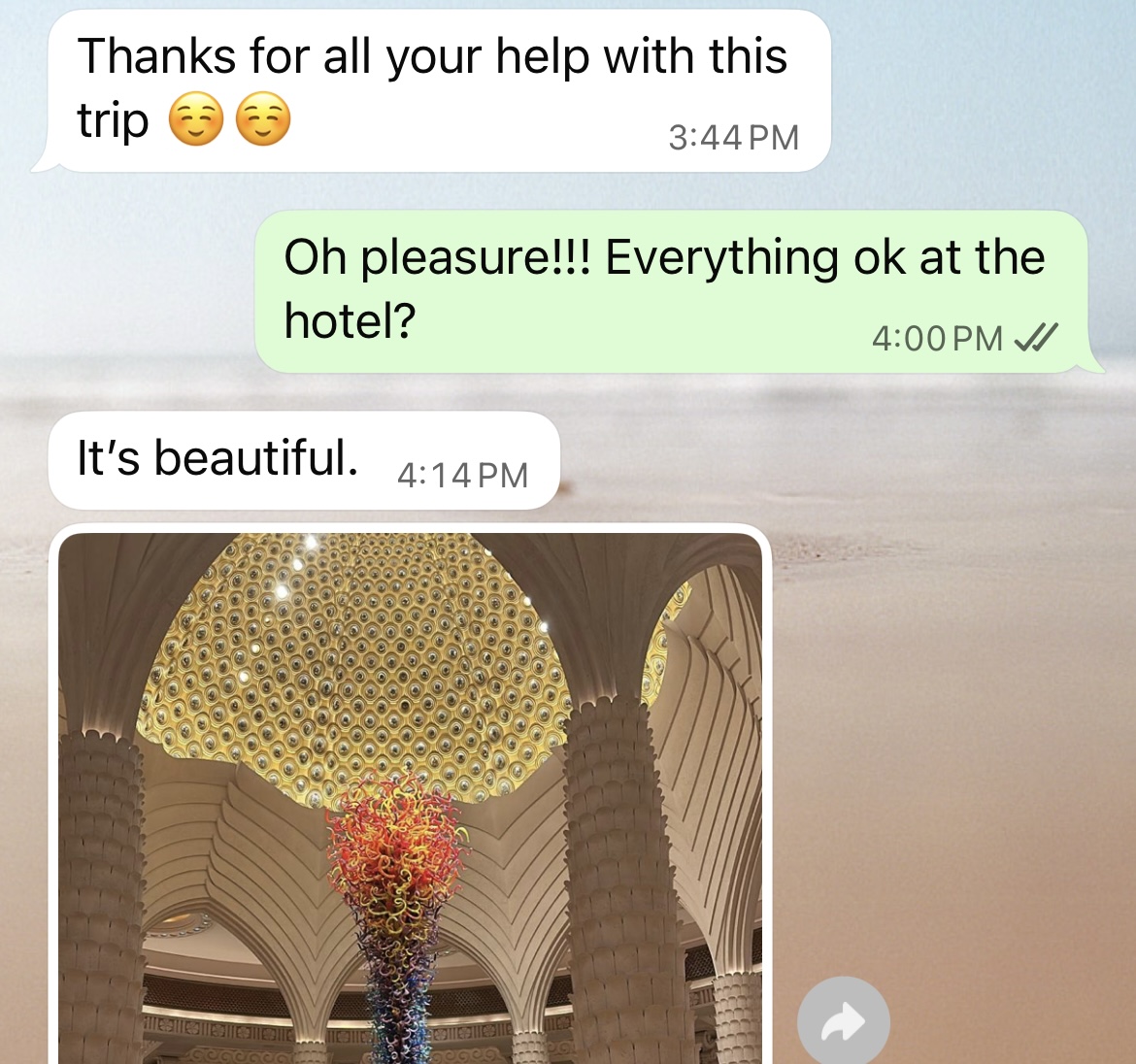 Here's alt text for the image:
"A stunning sculptural chandelier installation in a luxury hotel lobby featuring a large dome-shaped canopy covered in golden-yellow circular glass elements, with a dramatic cascading column of colorful hand-blown glass in vibrant reds, oranges, yellows, and blues flowing down from the center. The sculpture is set against ornate Art Deco-style architectural columns with geometric chevron patterns in cream and beige tones.