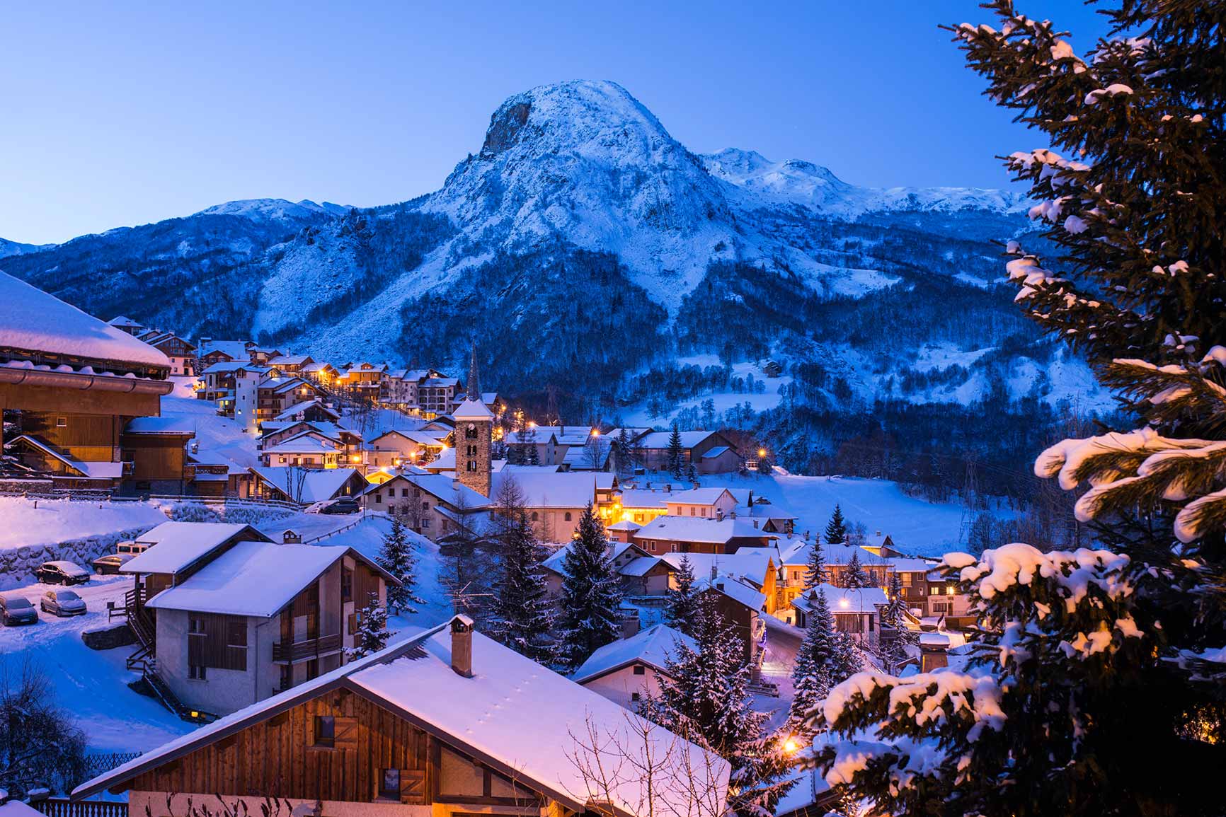 Twilight view of Saint-Martin-de-Belleville in the French Alps, with snow-covered chalets, a church tower, and surrounding mountains glowing under evening lights.