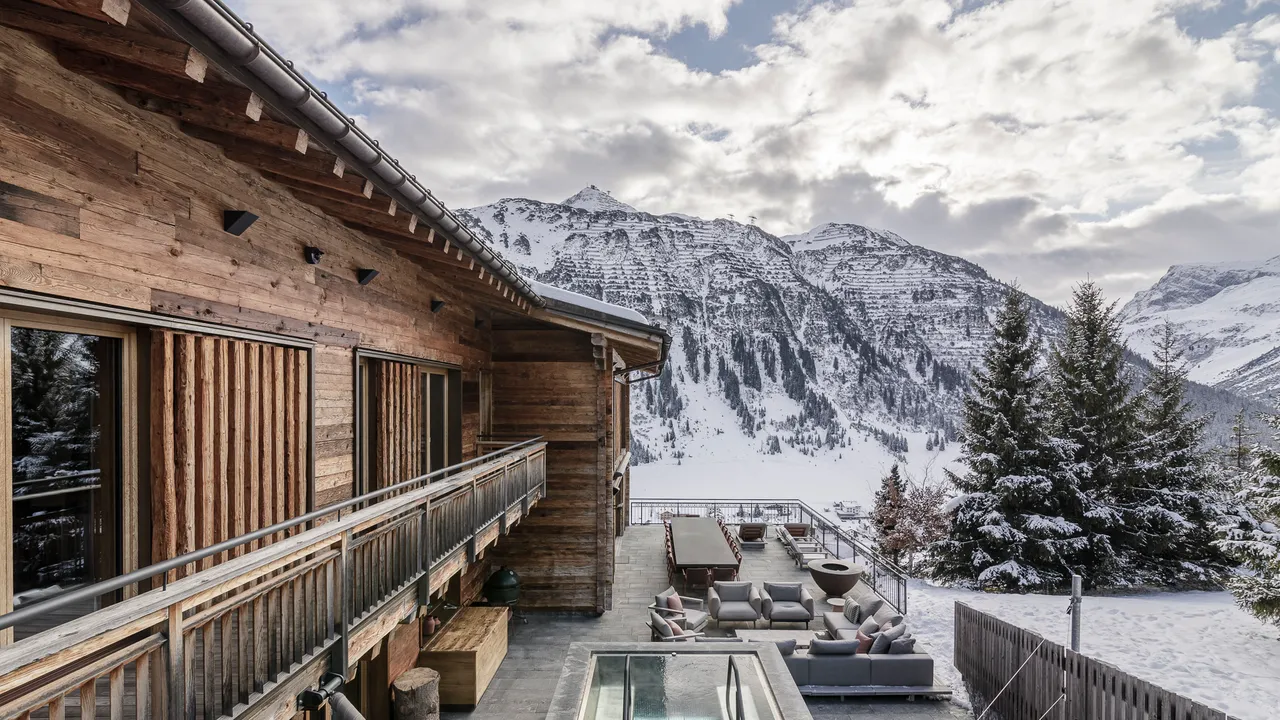 Luxury ski chalet in Lech, Austria, featuring a modern terrace with outdoor seating and mountain views overlooking snow-covered peaks.