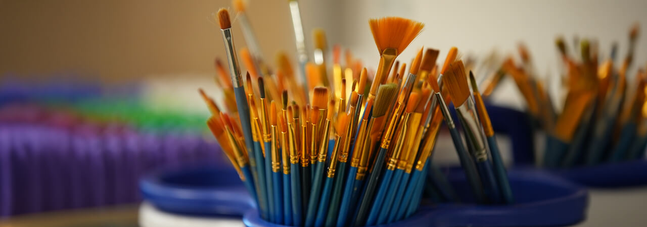 Close-up of various art paintbrushes with orange bristles standing upright in blue containers.