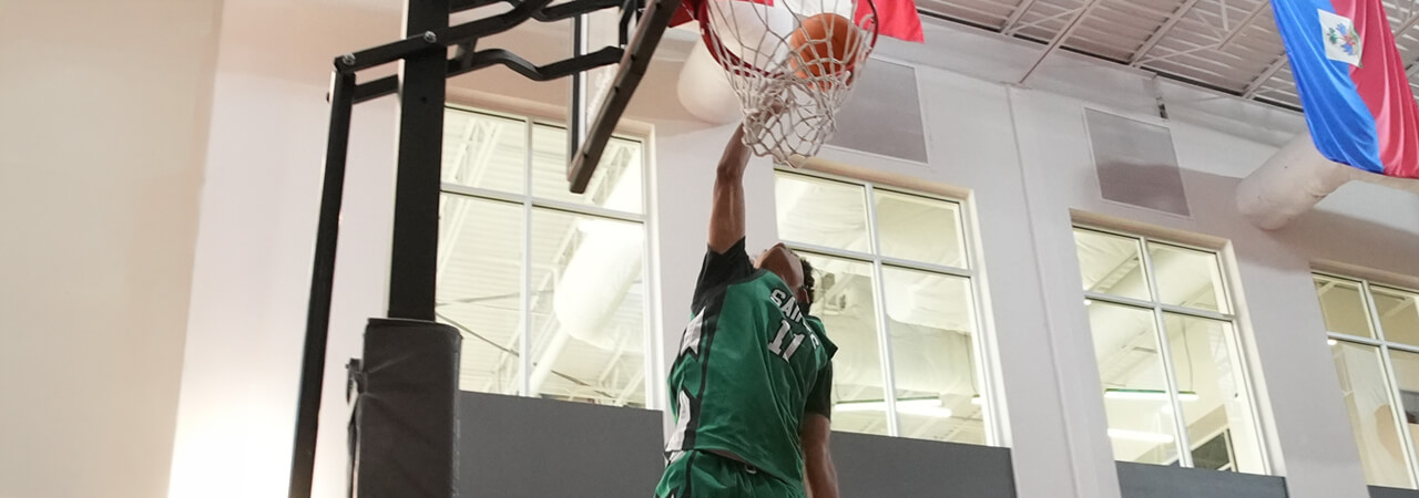 Basketball player wearing green jersey dunking the ball into the hoop indoors.