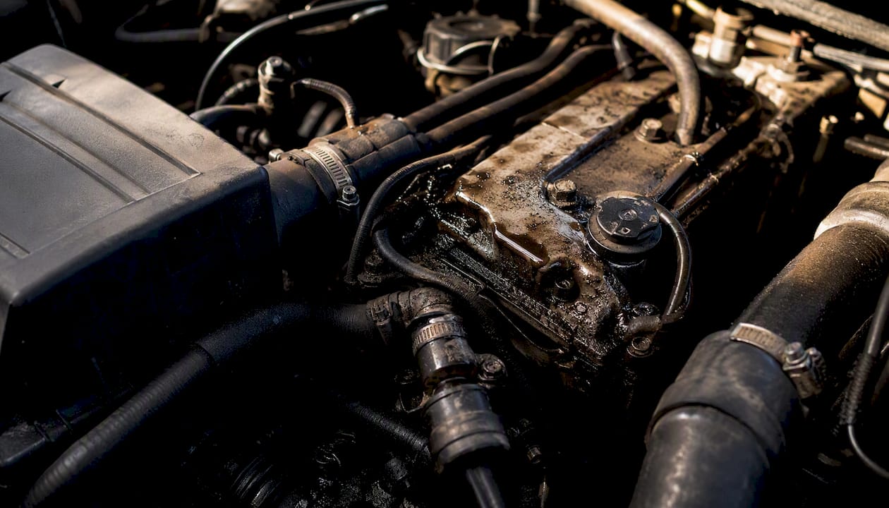 Close-up of used car engine bay showing grime with wet spots