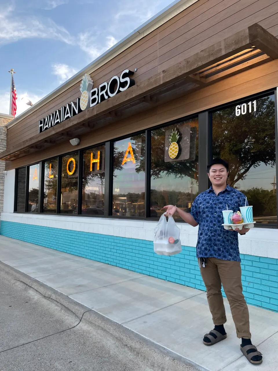 A picture of a happy customer standing outside of a Hawaiian Bros location with their order.