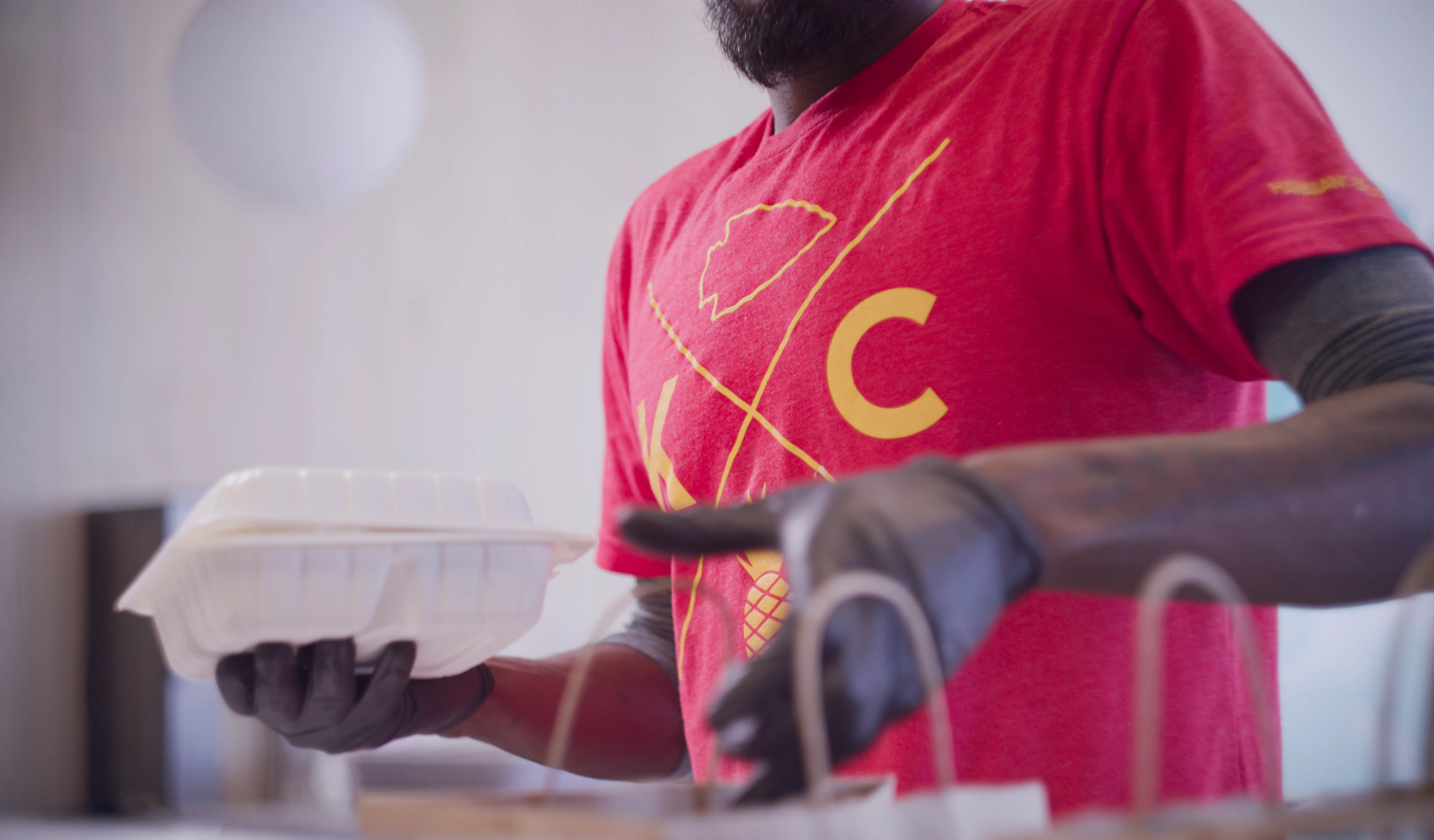 A Hawaiian Bros employee packing a page with a plate lunch.