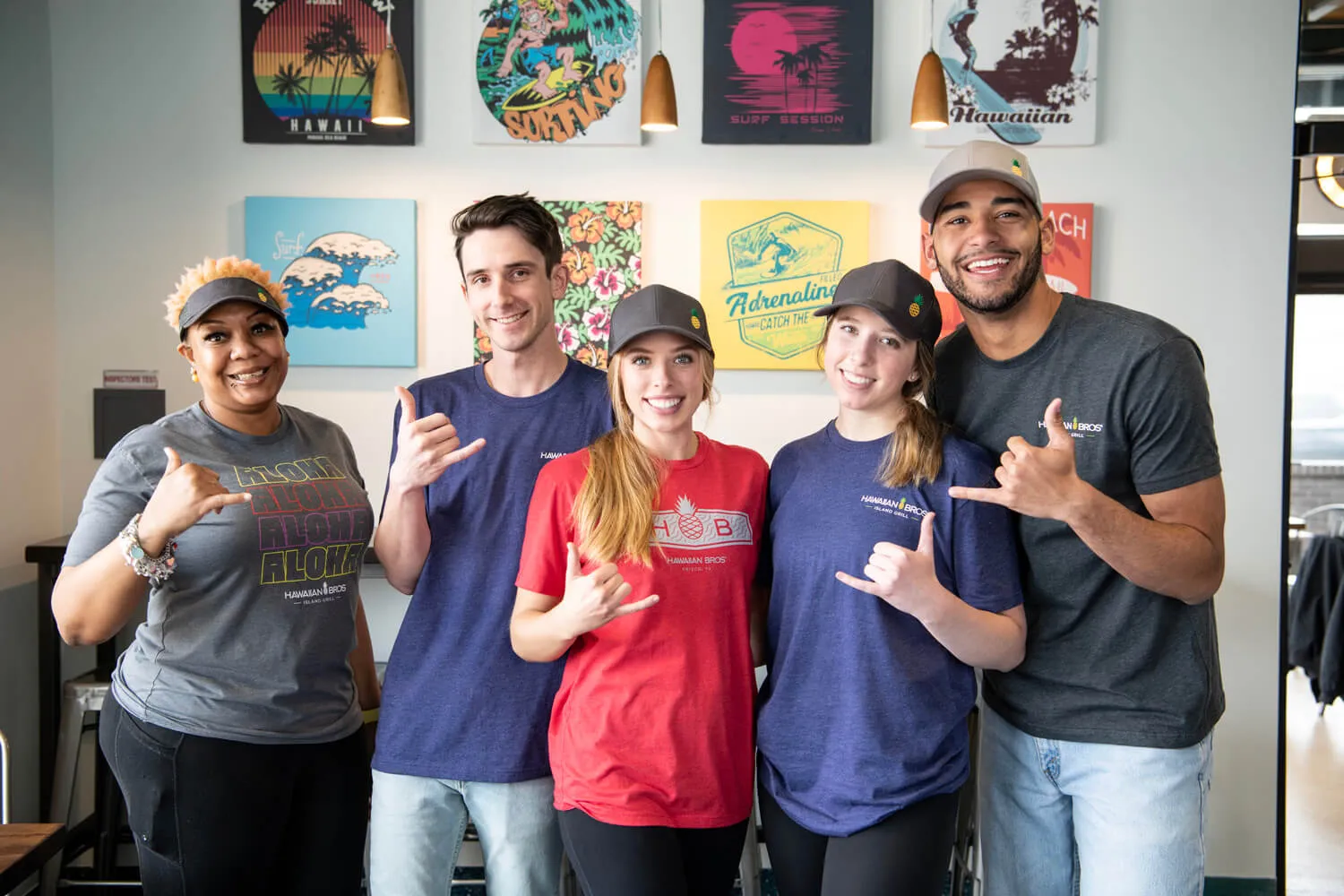 A group of Hawaiian Bros employees standing together and holding up shakas. 