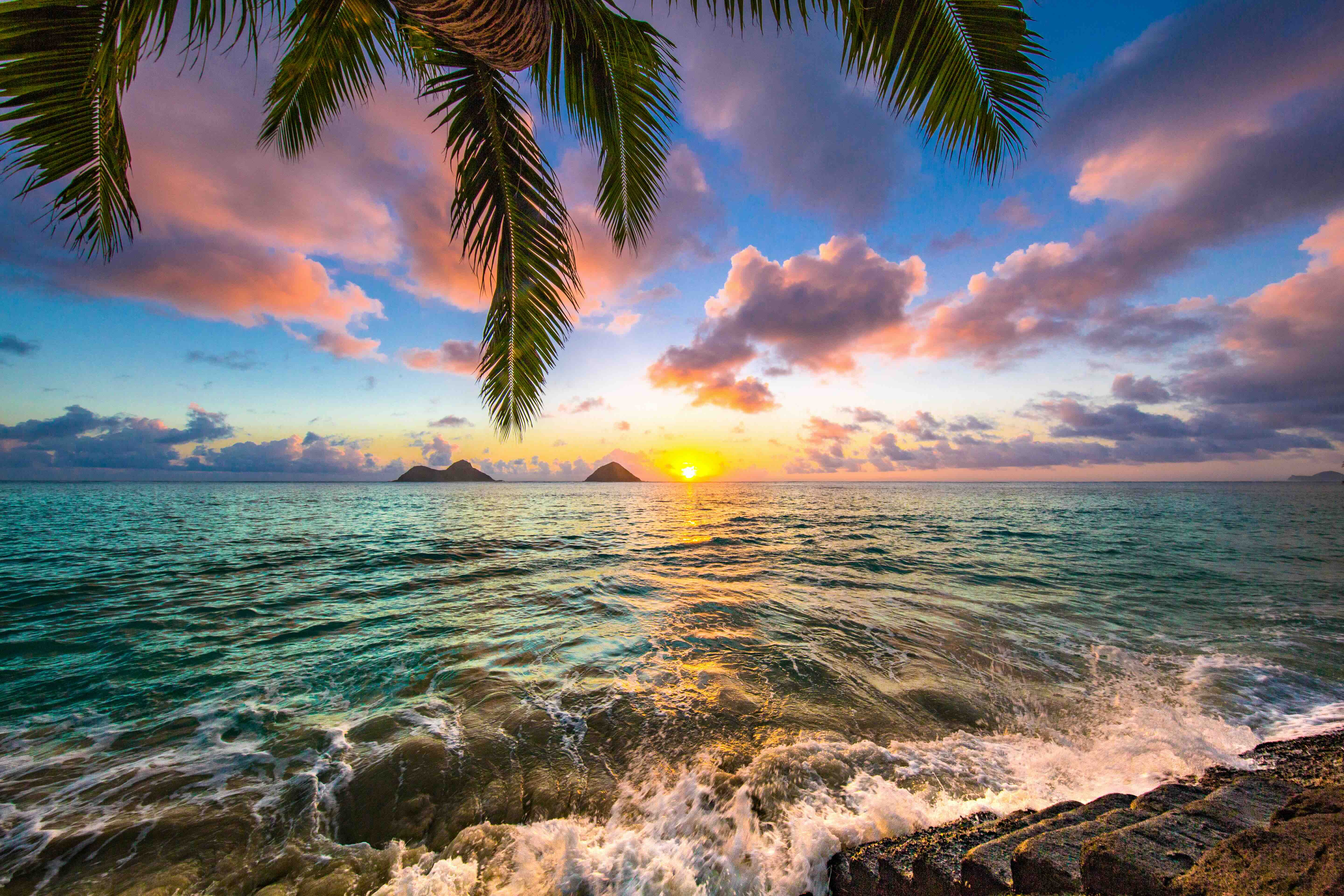 The ocean wave breaking on the sand with the Mokulua Island in the distance at sunset. 