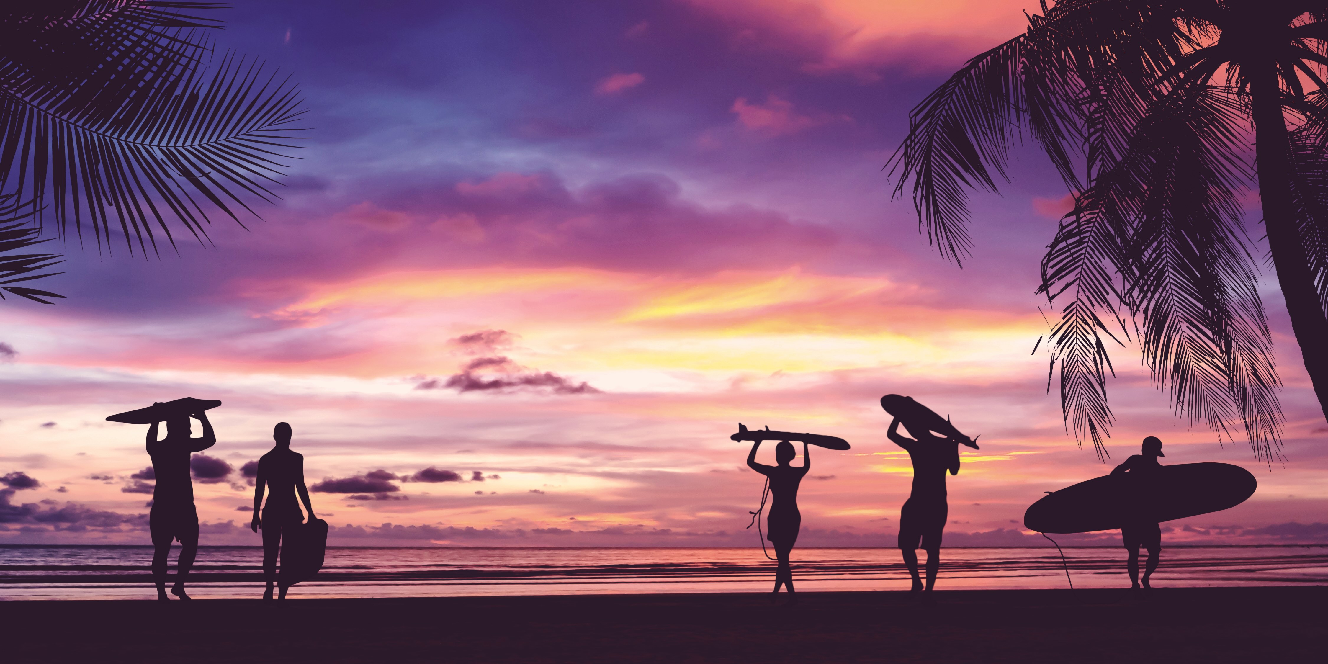A group of people coming back from surfing with a purple and pink sunset in the background.