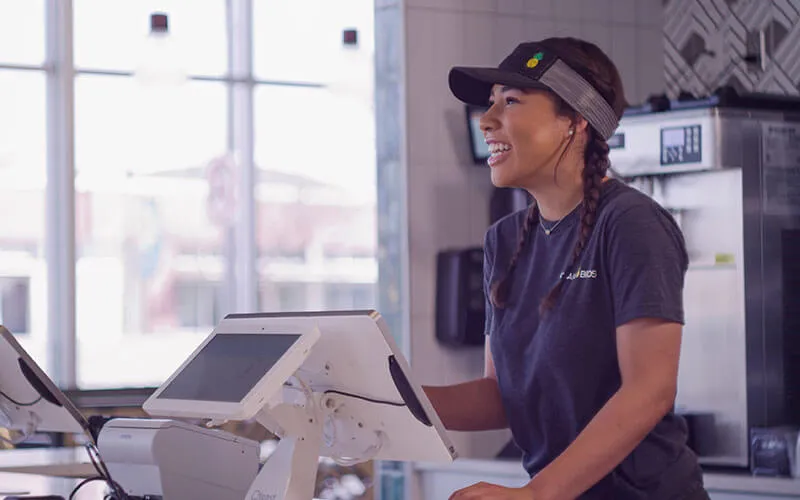 A smiling Hawaiian Bros cashier serving a customer. 