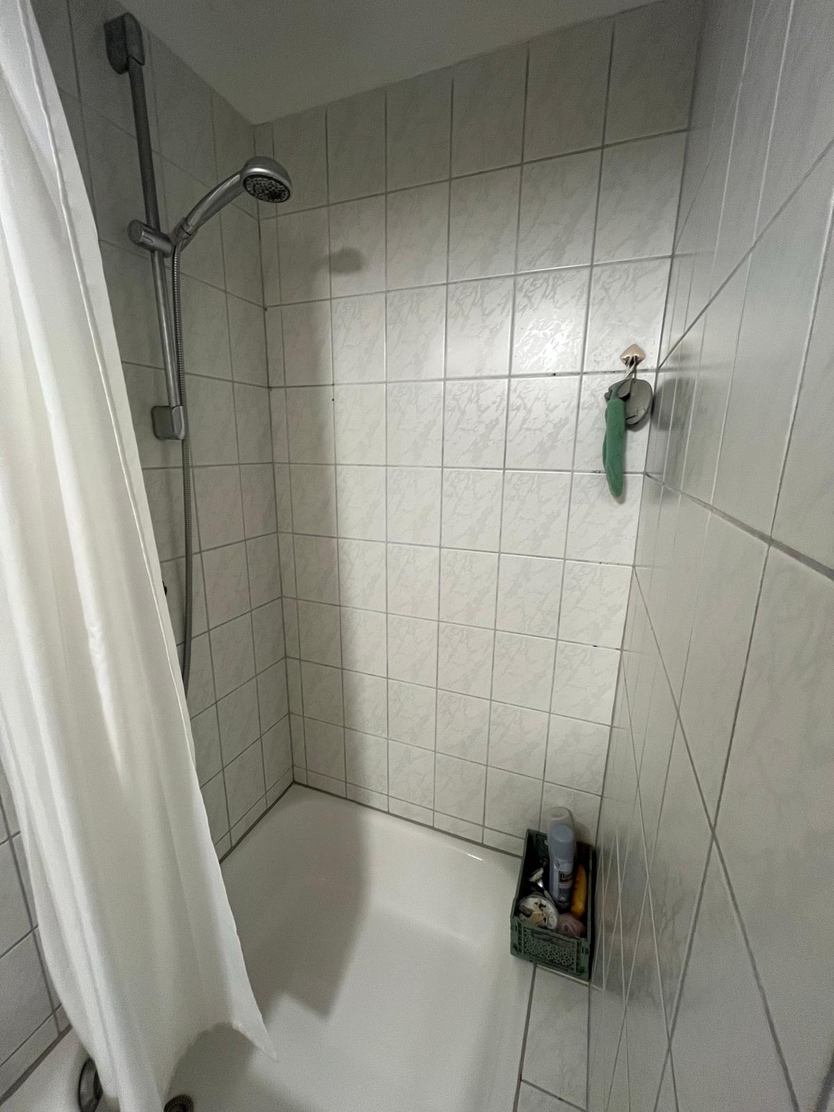 Badewanne mit Dusche und weißen Fliesen im Badezimmer der Wohnung in Aachen