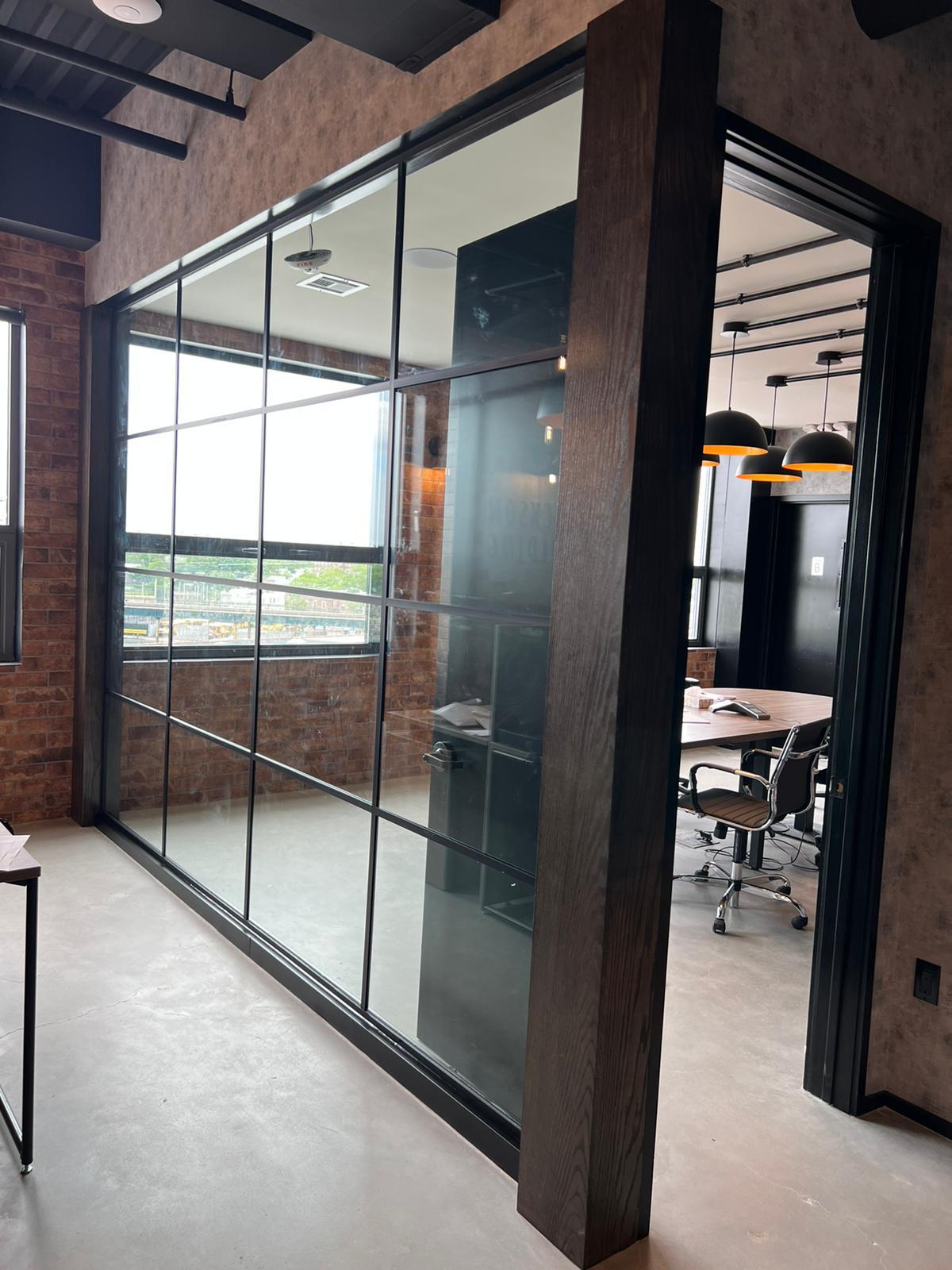 Modern office interior with glass partition, exposed brick walls, and a conference room with chairs and hanging dome lights.