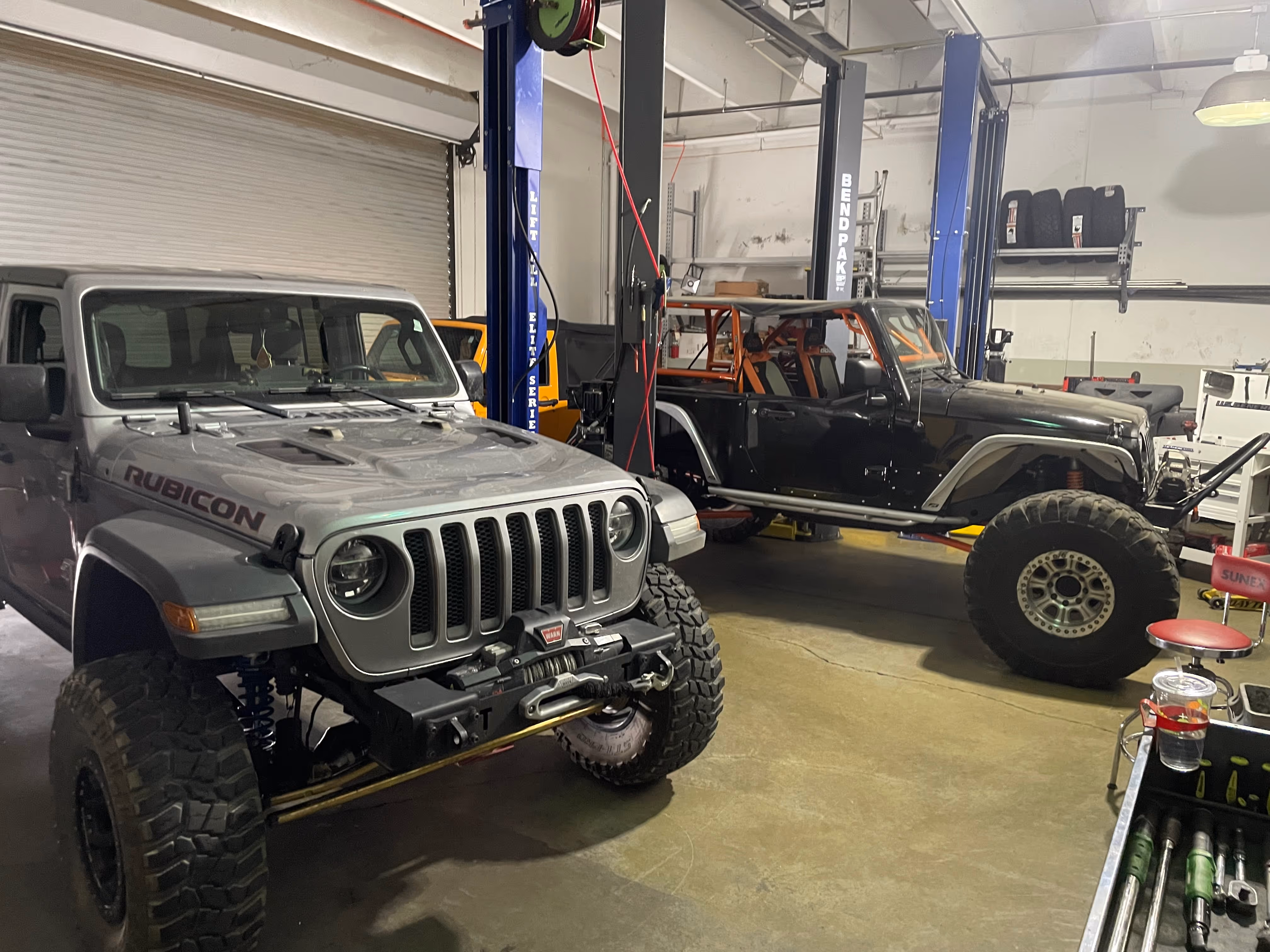 Two modified Jeep Wranglers with large tires in an auto repair shop