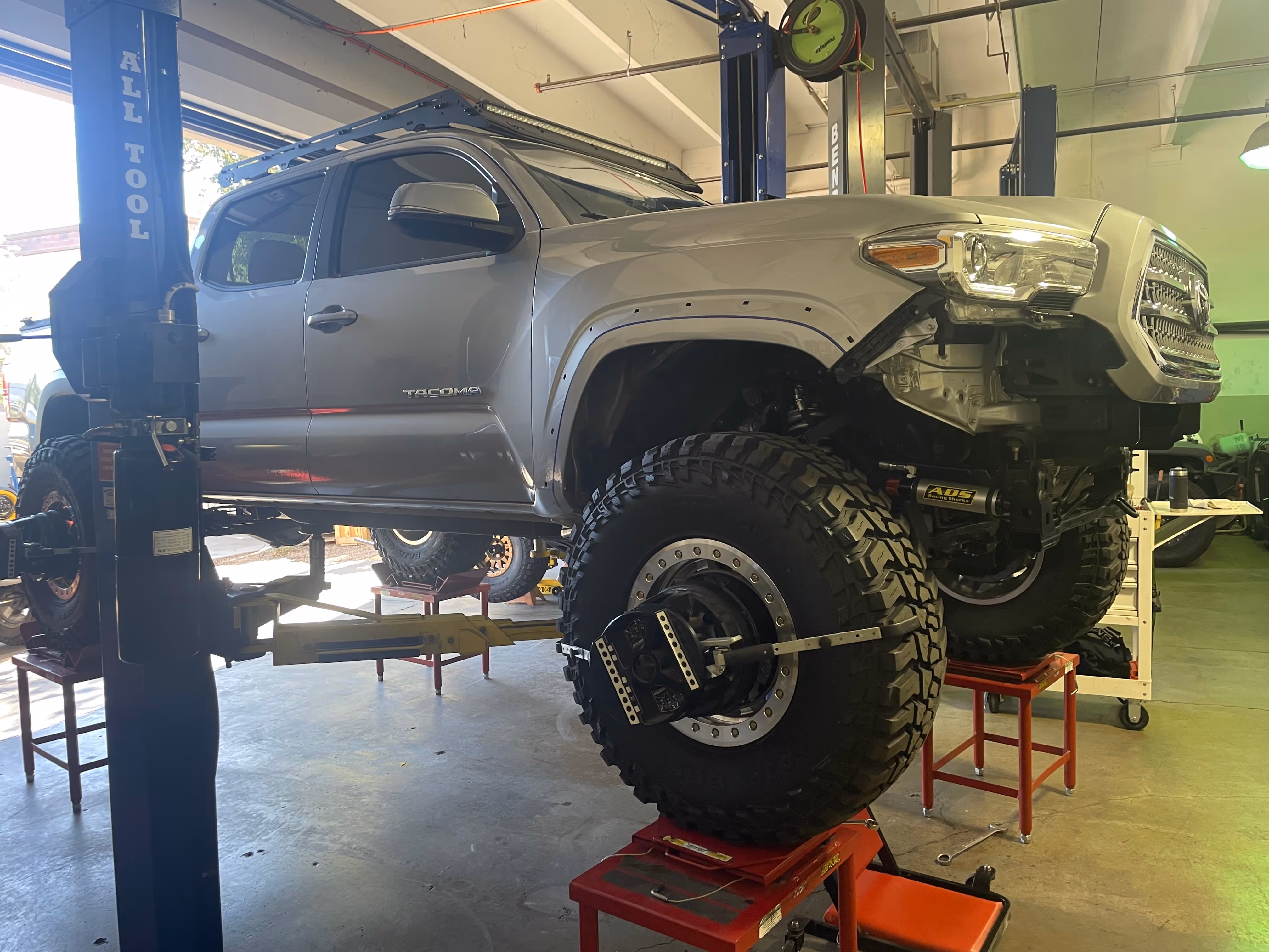 Toyota Tacoma truck lifted on jack with large off-road tires in garage