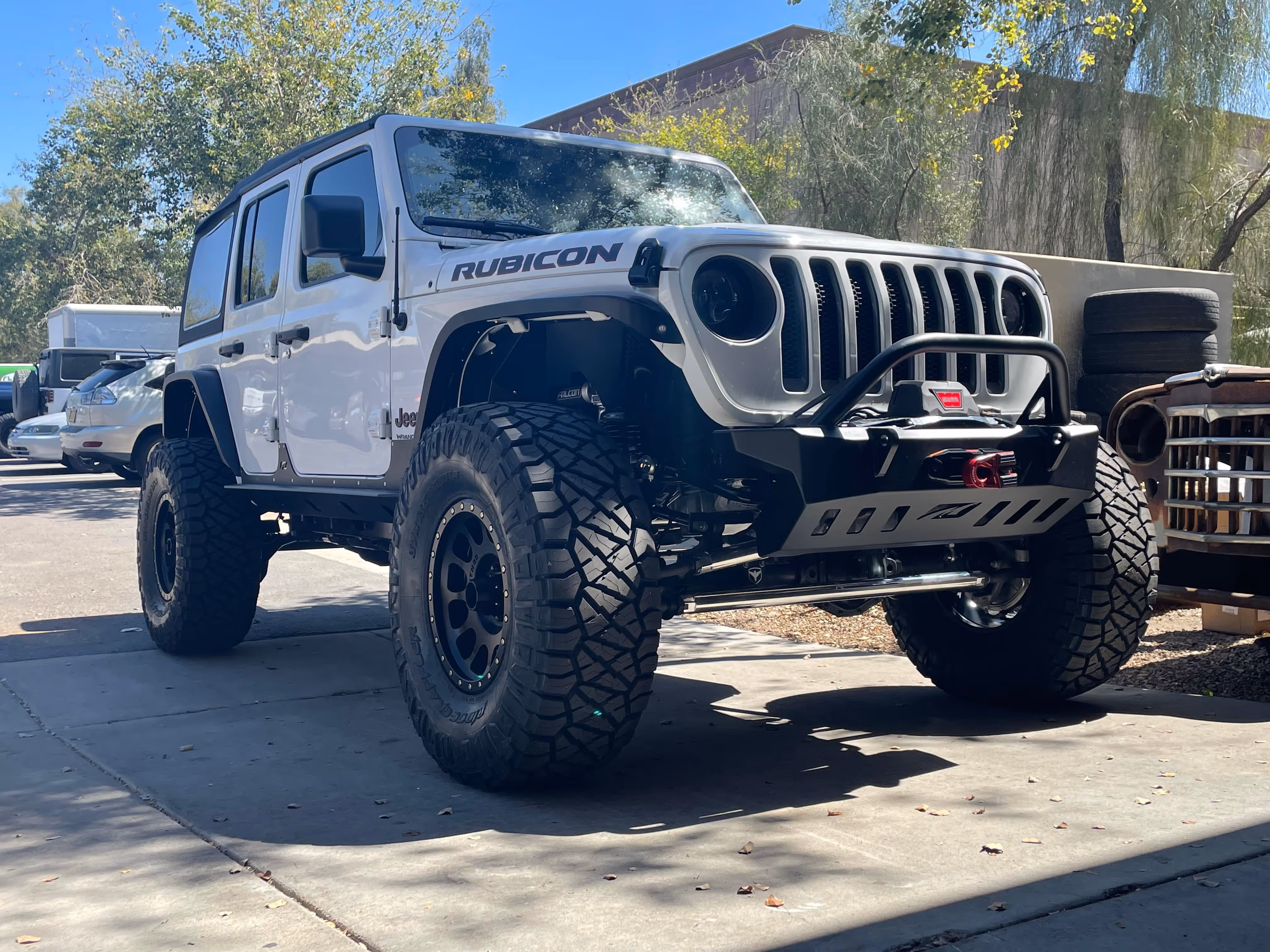 White Jeep Rubicon with large off-road tires and rugged bumper parked outside