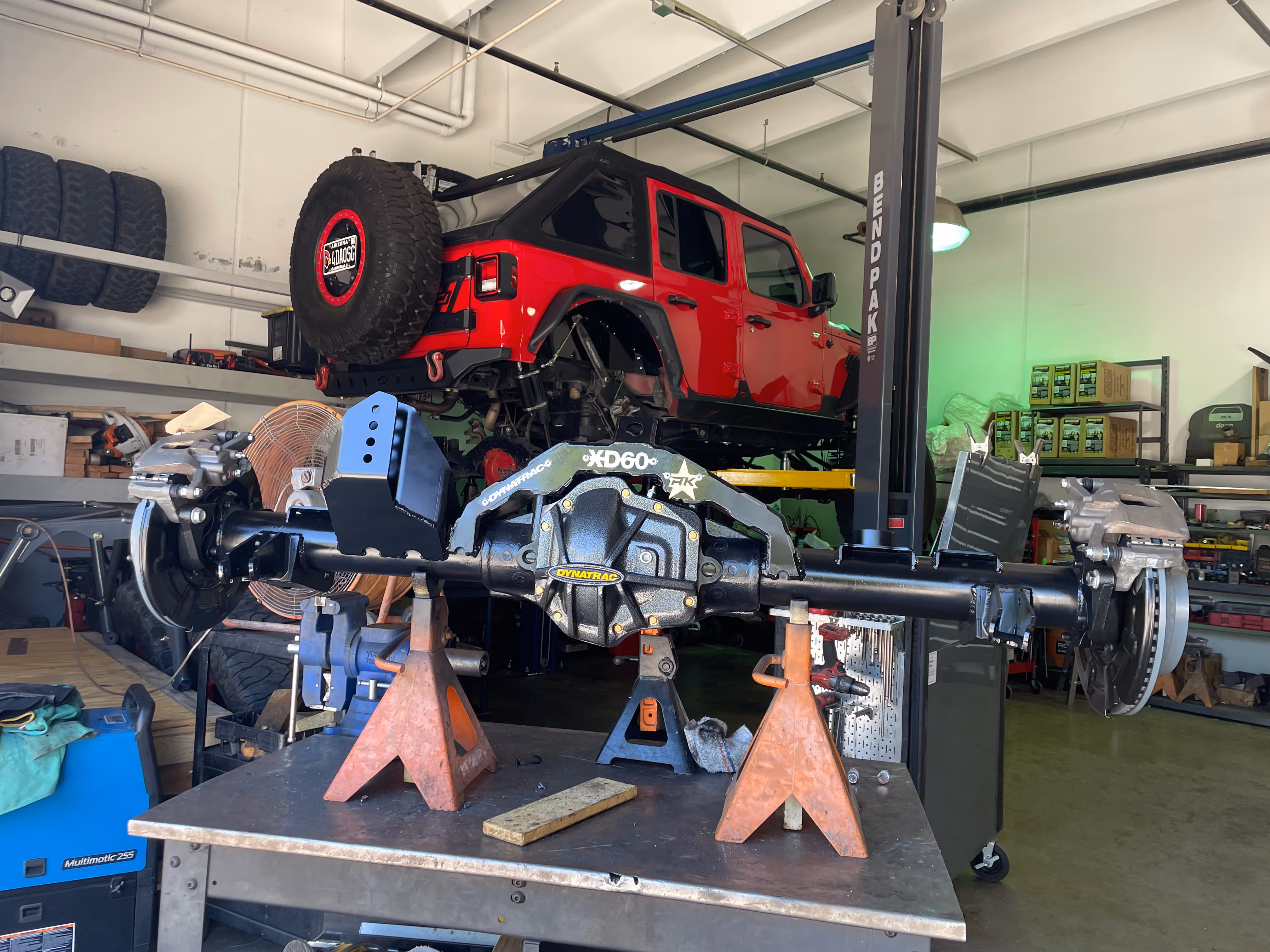 Red Jeep Wrangler on lift with axle removed in automotive repair shop