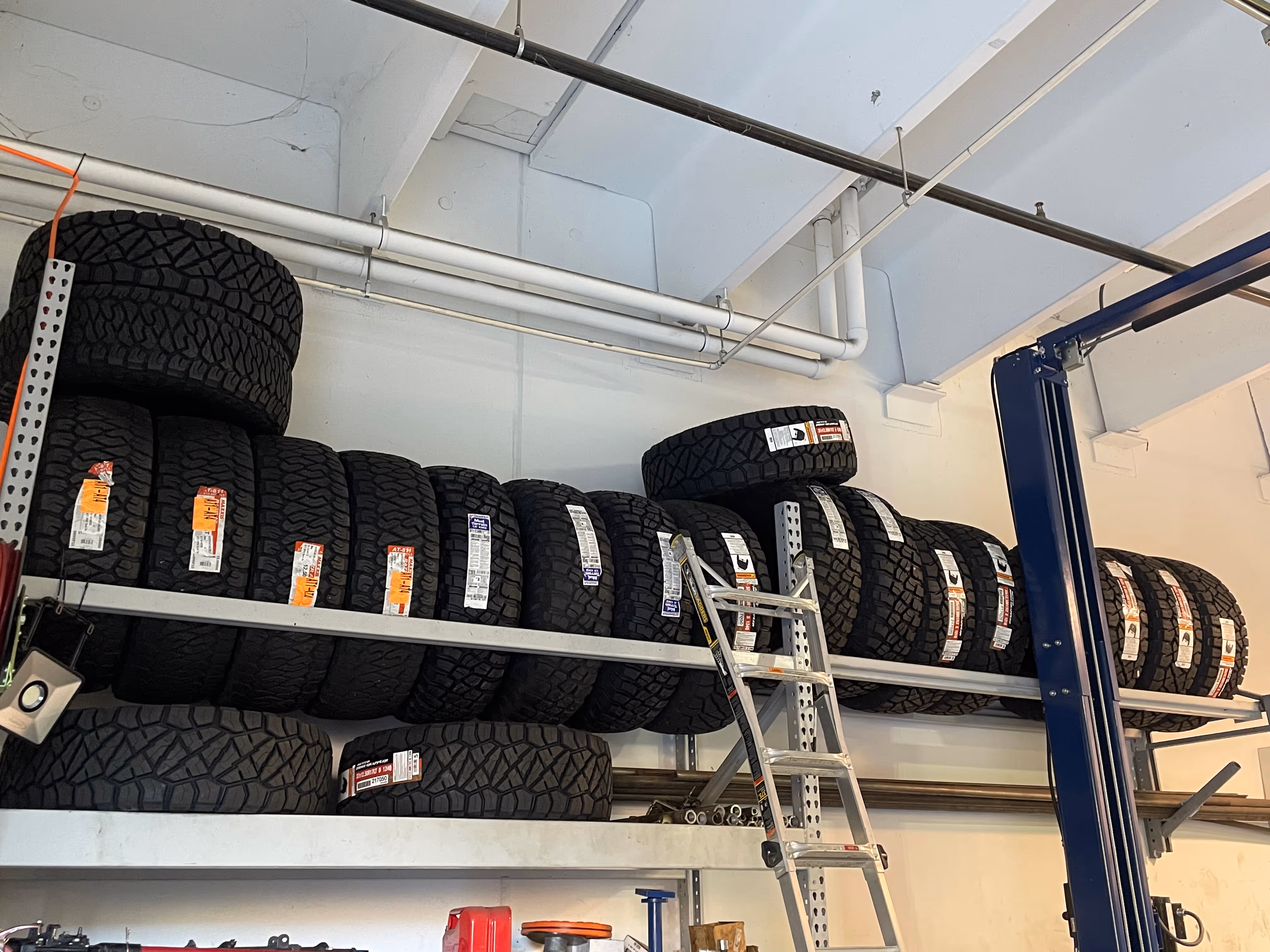 Rows of black off-road tires stacked on metal shelves with ladder