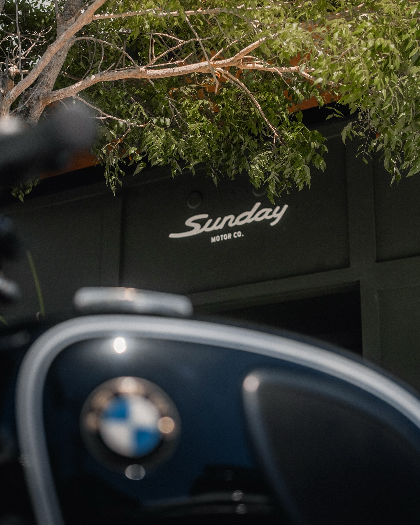 Sunday Motor Co West Palm Beach, Florida location storefront with the gas tank of a BMW motorcycle in frame