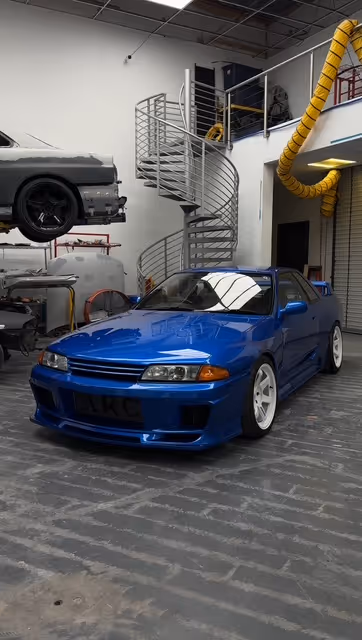 Blue Nissan Skyline GT-R in automotive workshop with spiral staircase