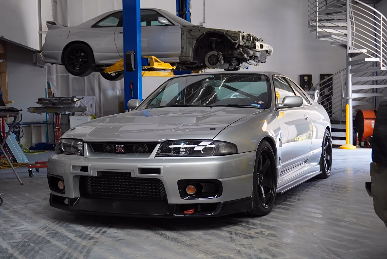 Silver Nissan Skyline GT-R in automotive workshop with car lifted