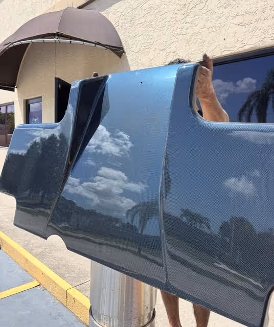 Blue car door reflects cloudy sky and trees on sunny day