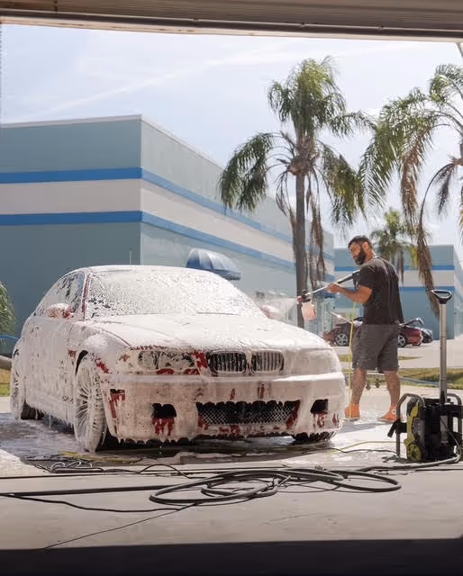 Man washing foam-covered BMW at self-service car wash with palm trees