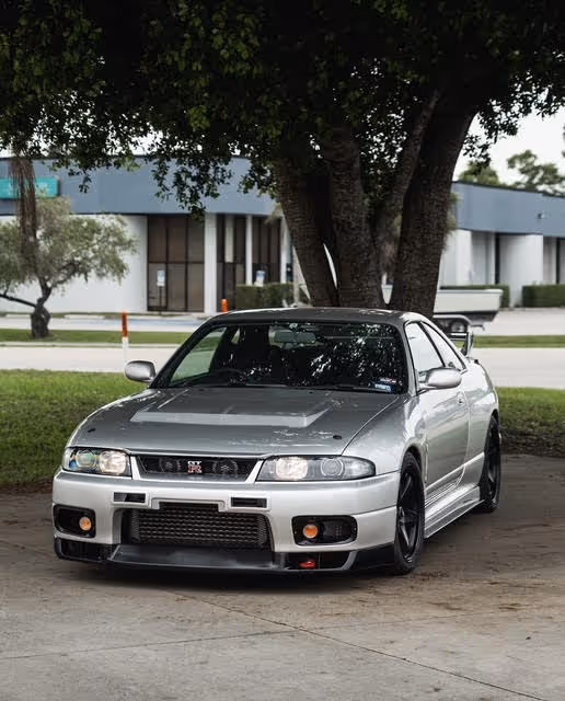 Silver Nissan Skyline GTR parked under tree near modern building
