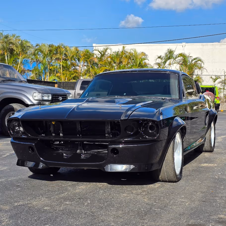 Black classic Ford Mustang with custom wheels parked in tropical setting