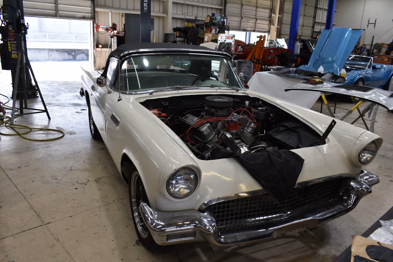 White vintage Ford Thunderbird with open hood in auto repair shop