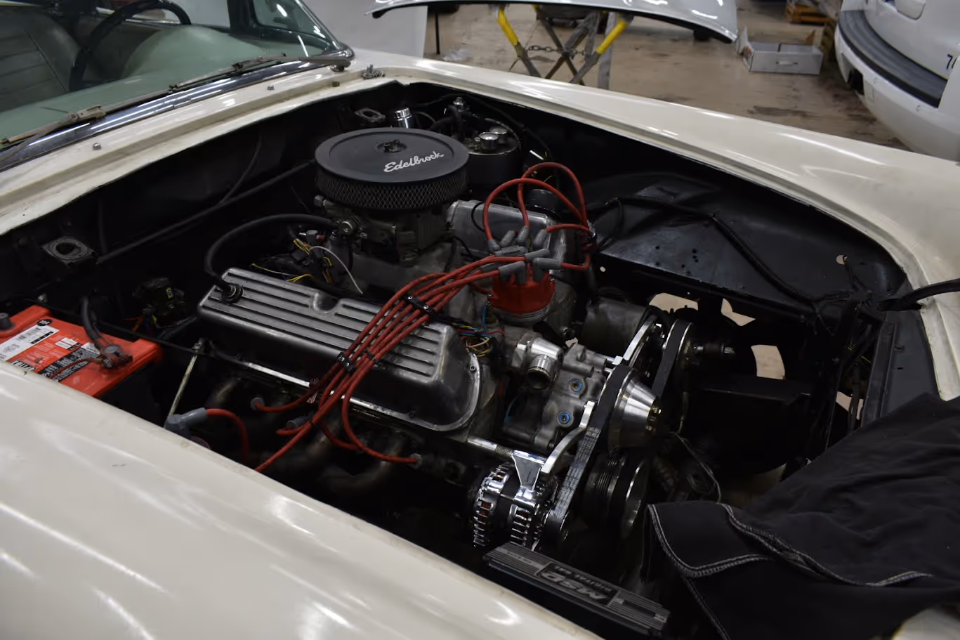 Vintage car engine bay with red wires and Edelbrock air filter