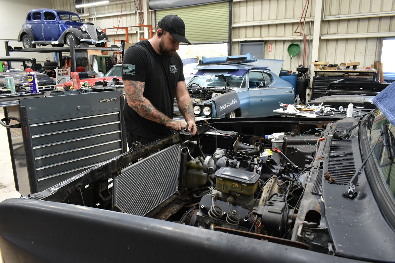 Mechanic repairing classic car in workshop with vintage vehicles