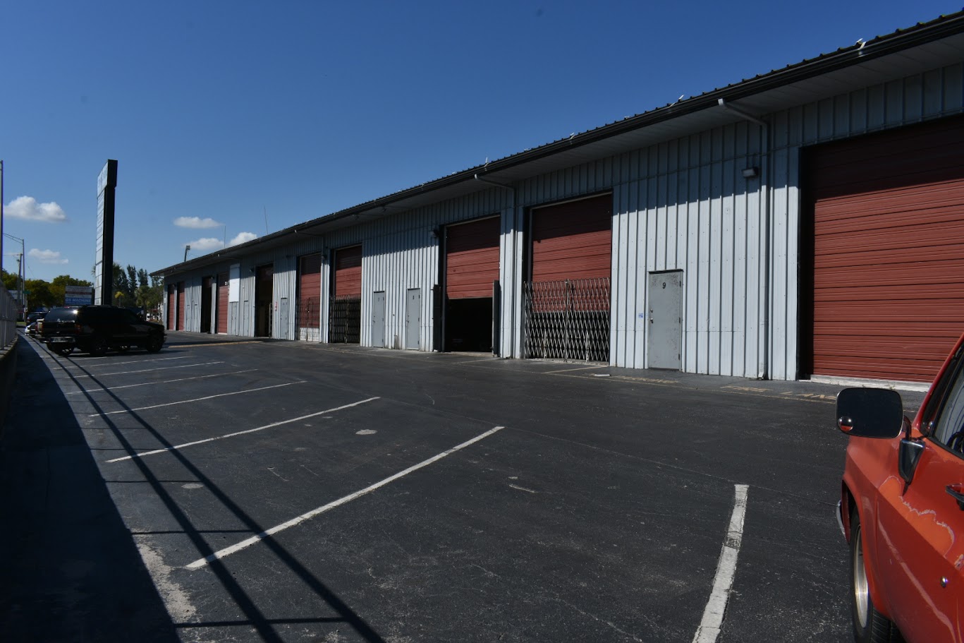 Storage units with red and white doors and parking lot on sunny day