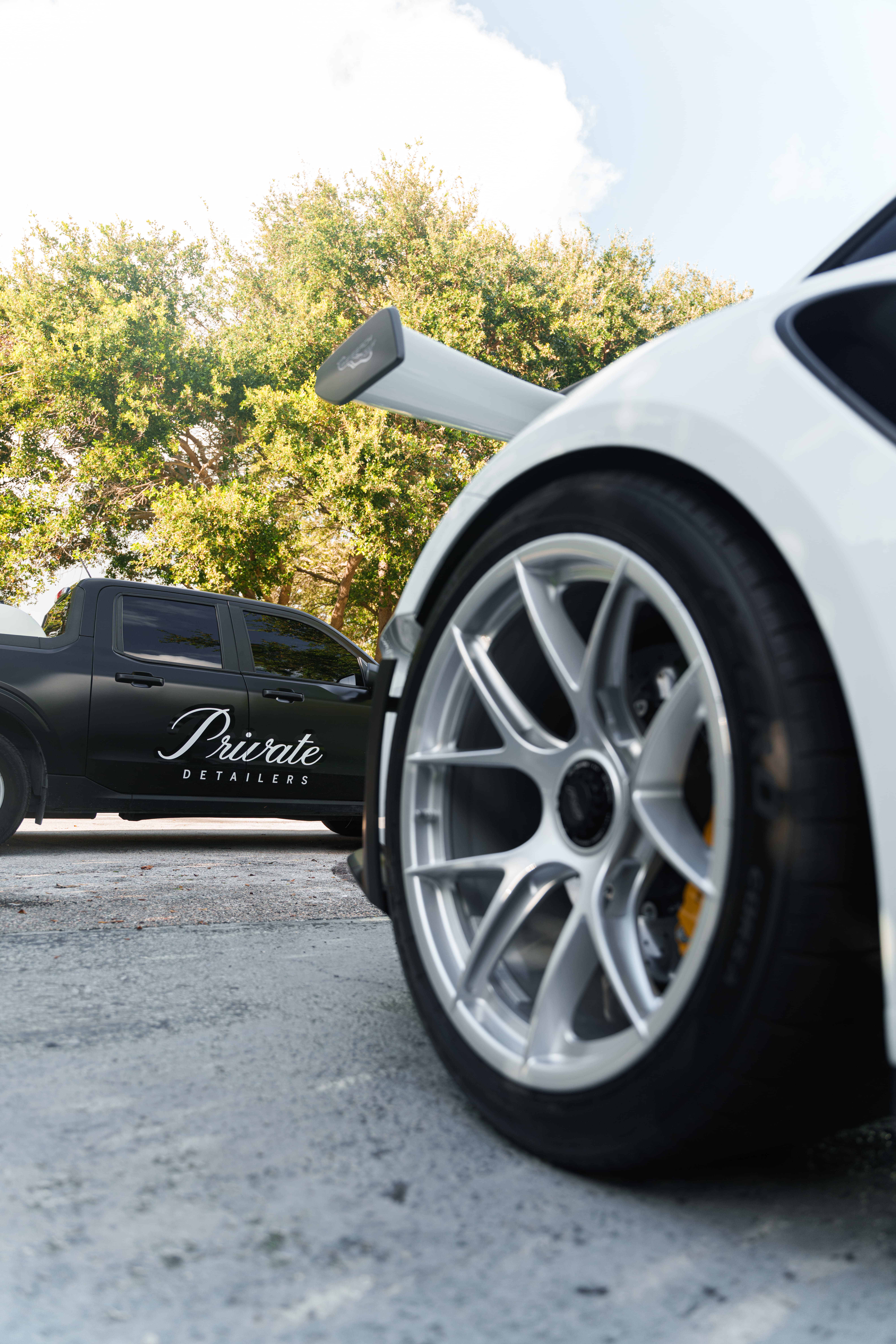 Wheel and passenger quarter panel of a white Porsche with the Private Detailers truck behind it