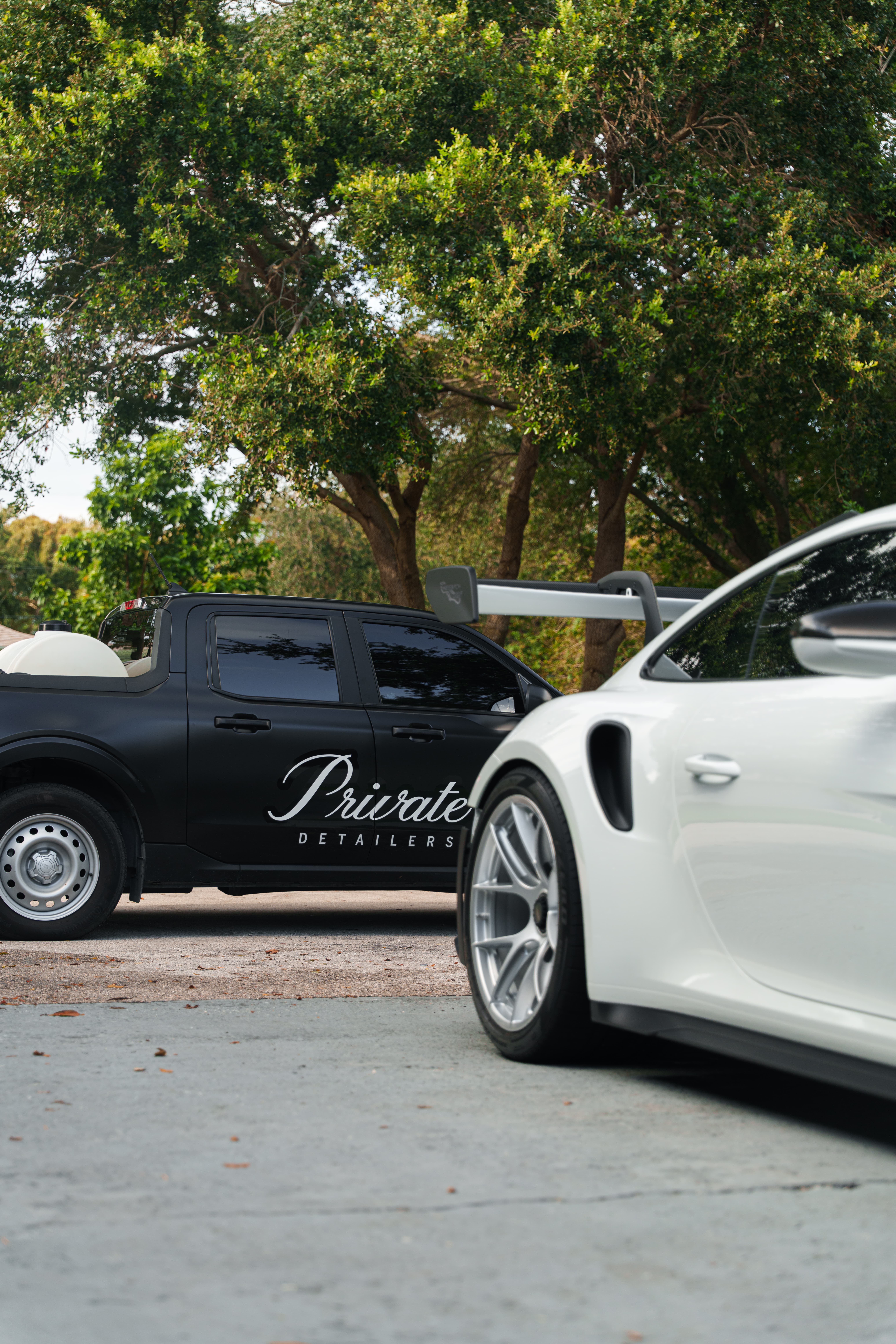 Black truck with the Private Detailers logo behind a white Porsche
