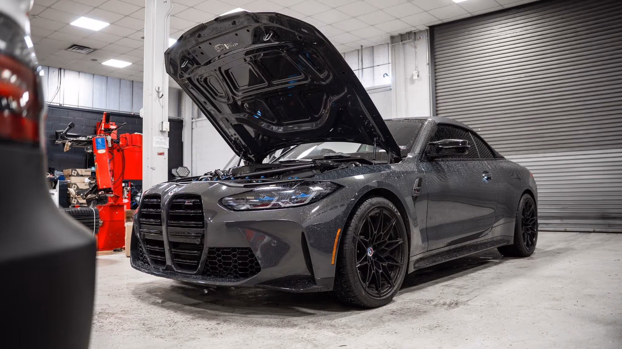 Gray BMW M4 with open hood in automotive workshop