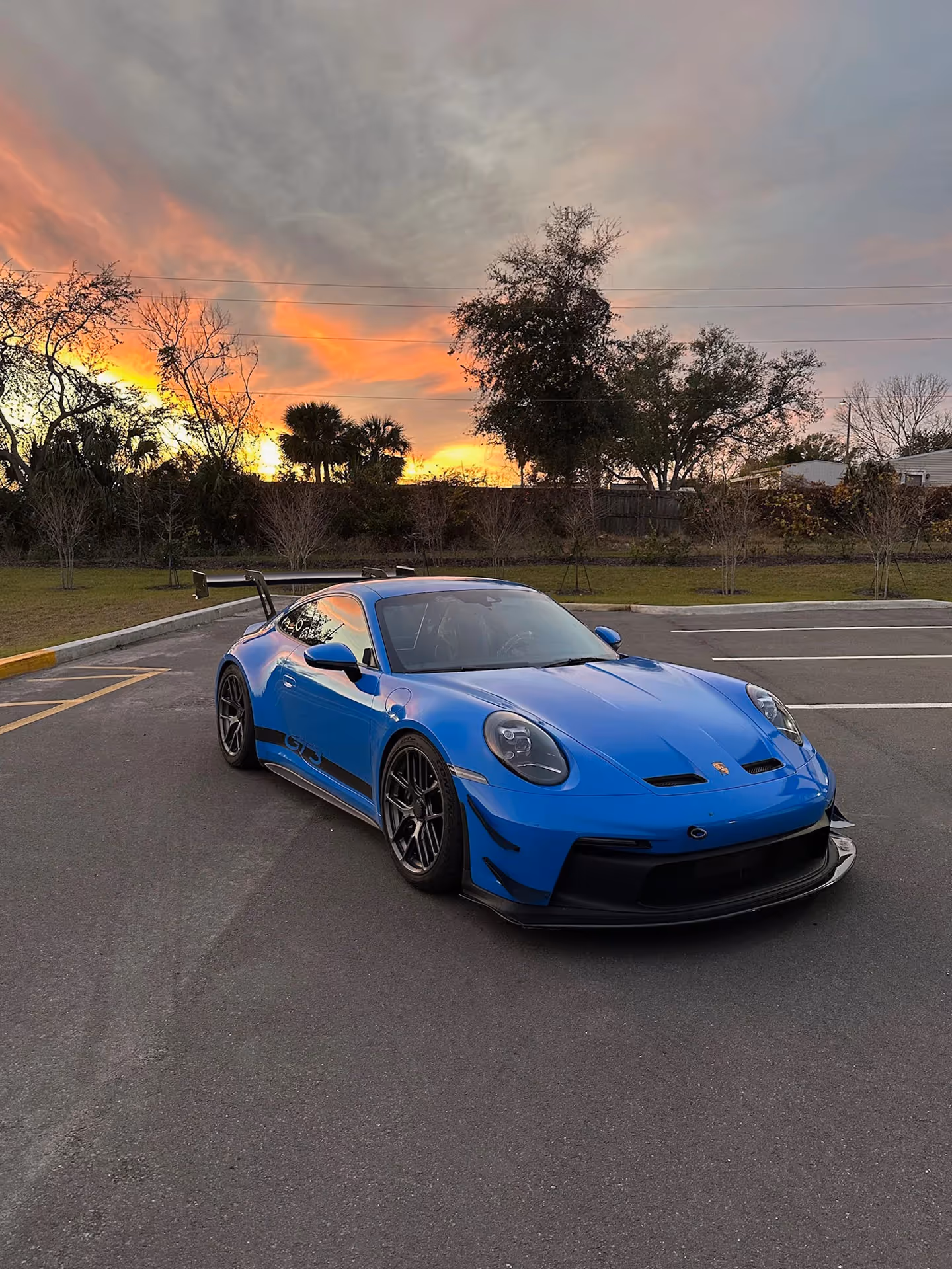 Blue Porsche GT3 RS parked in lot with dramatic sunset sky